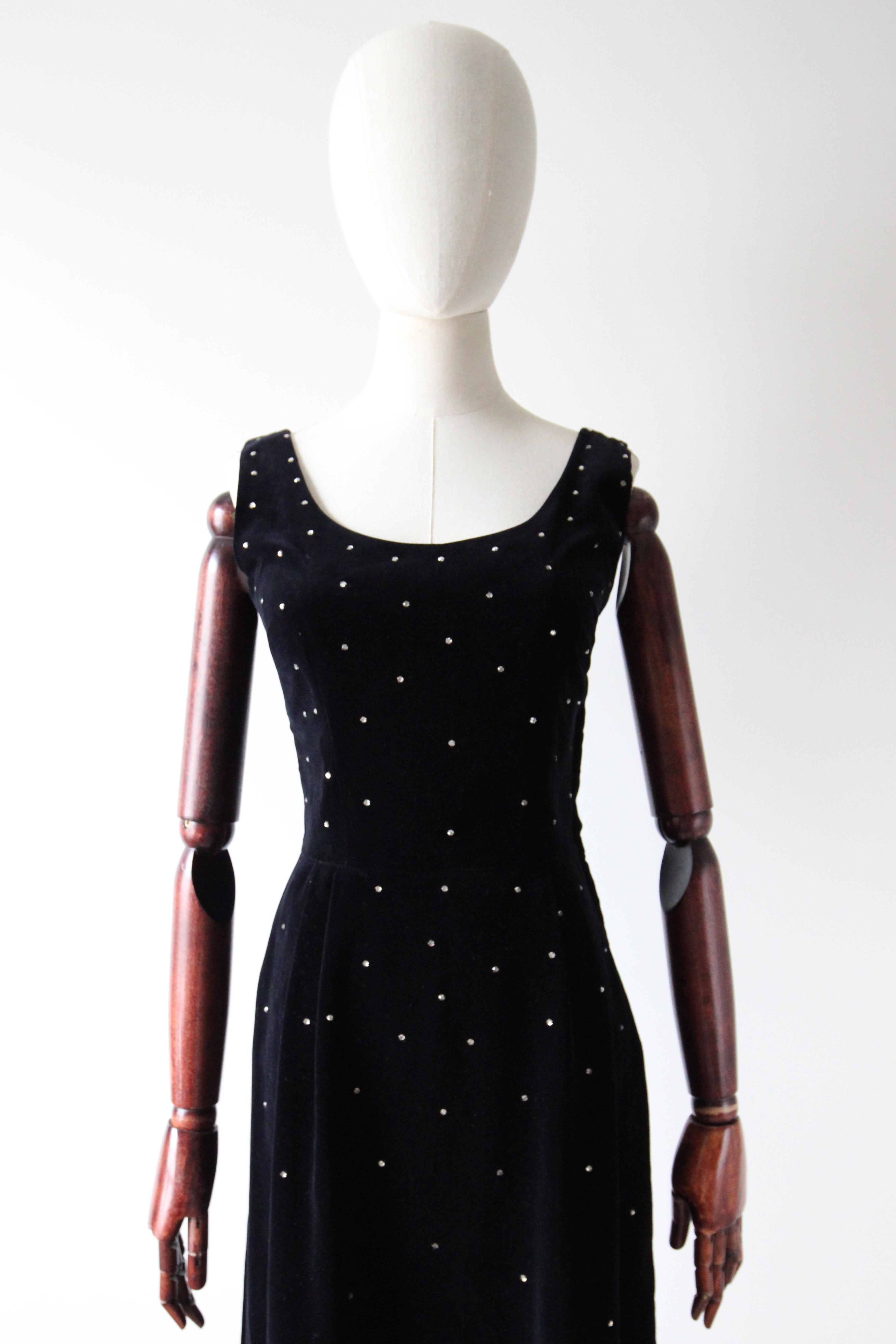 Rendered in the deepest shade of black velvet and embellished with silver claw set rhinestones, this original 1950's dress, is just the piece to add to your cocktail wardrobe. 

The rounded neckline of the dress is framed by medium width shoulder