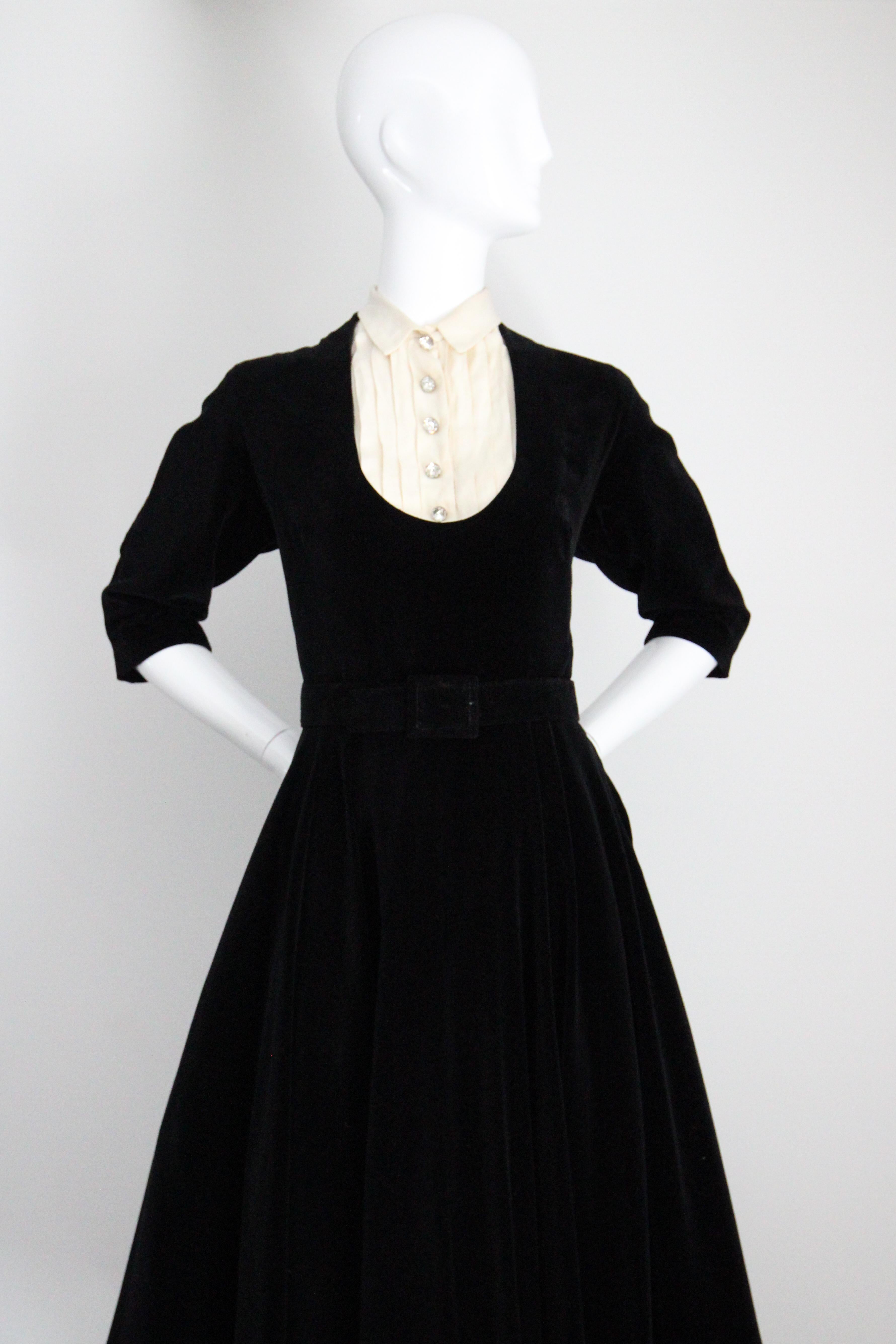 Rendered in a lustrous black velvet and accented by a cream cotton décolletage and statement silver rhinestone buttons, this original 1950's dress is sure to be a favourite in your seasonal collection.

The rounded neckline, rendered in the form of