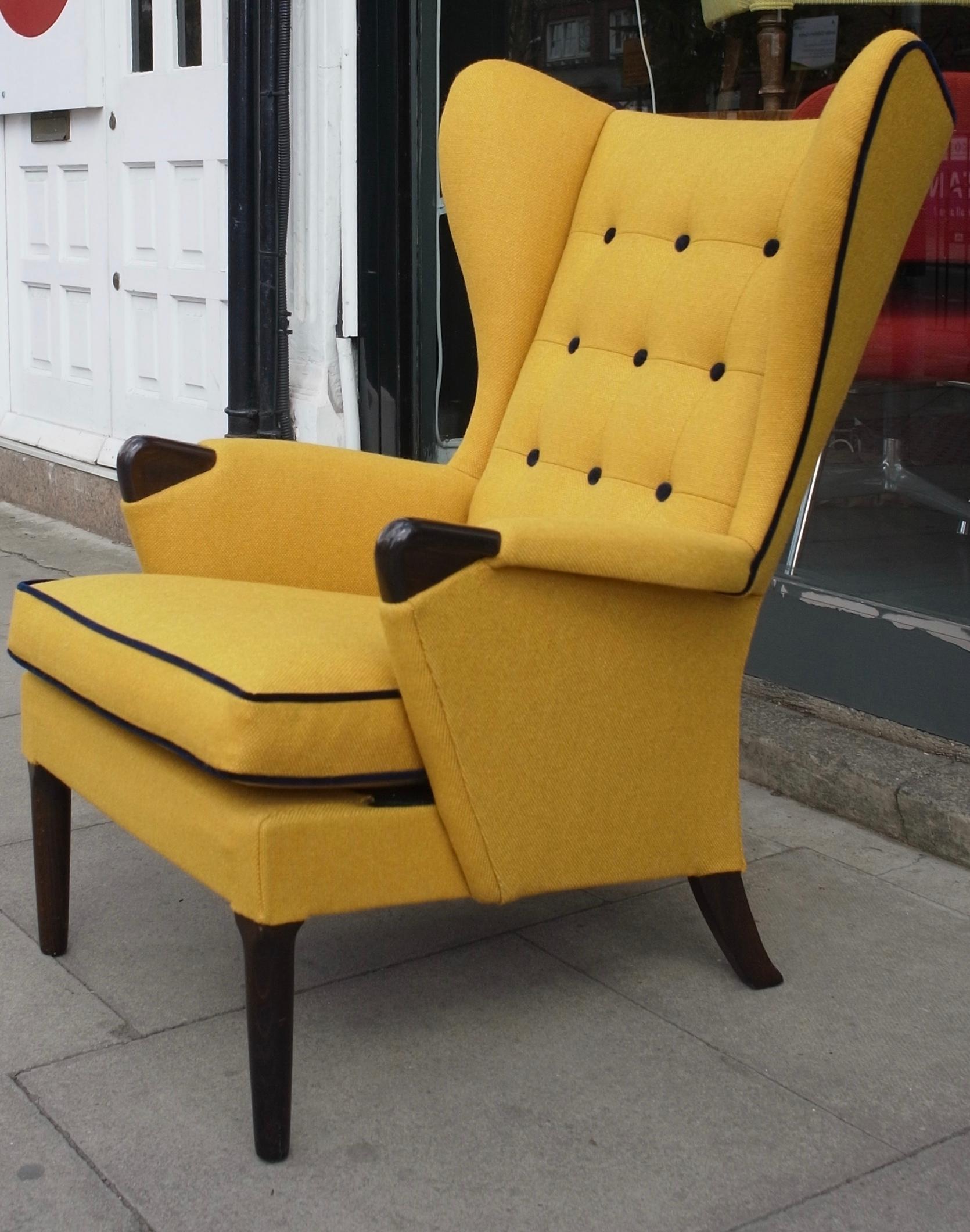 Ein sehr bequemer und stilvoller englischer Ohrensessel aus den 1950er Jahren mit Knöpfen.  Neu gepolstert in einem gelben Qualitätsstoff mit marinefarbenen Samtkedern und Knöpfen, die das elegante Profil des Stuhls betonen.  Die dunkel gefärbten