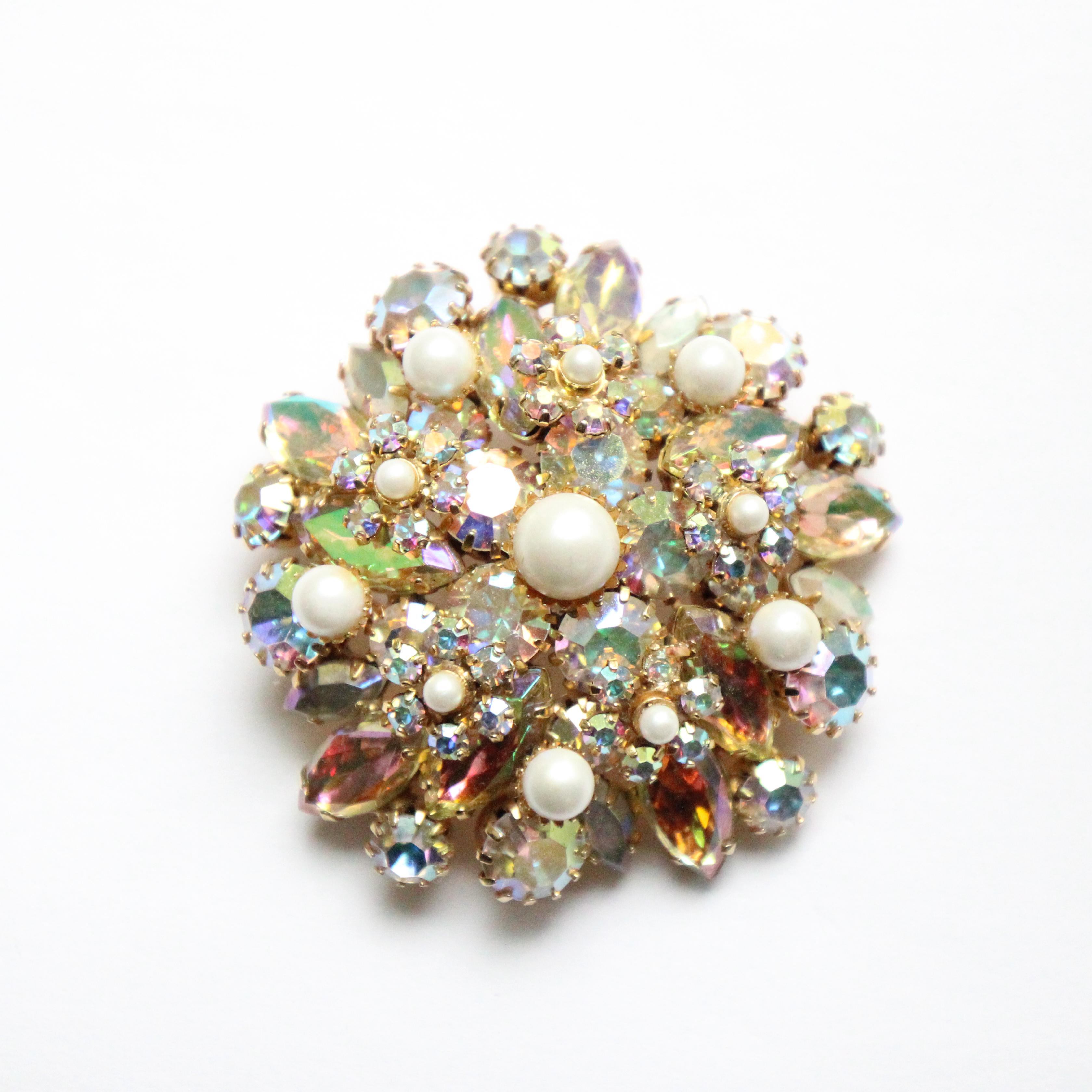 A sparkling beauty to behold. This original 1950's rhinestone brooch, on a gold toned domed metal base, embellished with layers on iridescent rhinestones and finished with decorative inset pearls in a scattered floral design,  is the perfect
