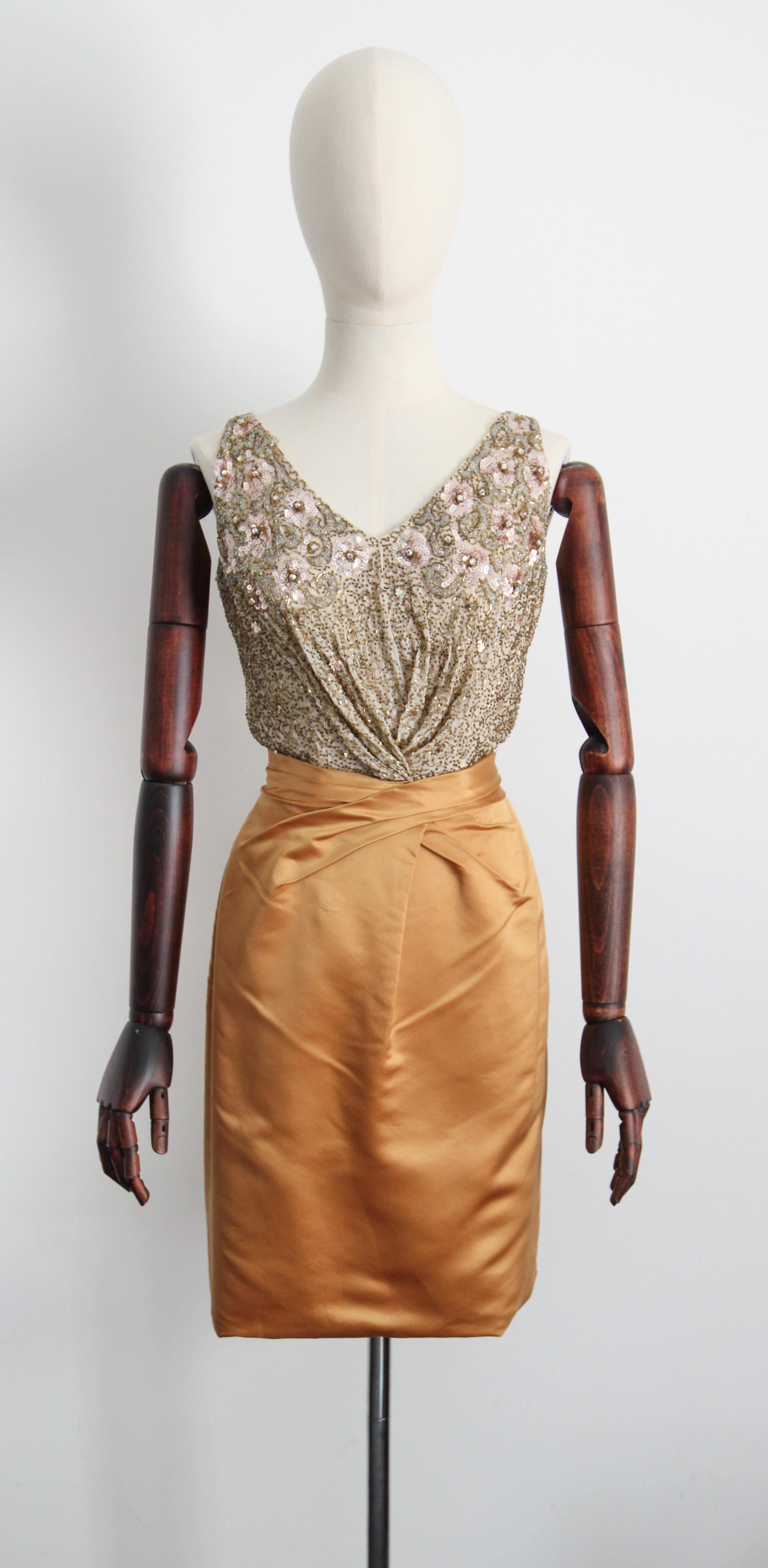 Rendered in a classic silhouette, this sumptuous 1950's Ceil Chapman dress, in a bold gold satin, contrasted by a cream silk bodice embellished with trailing gold glass bugle beads, contouring silk and pink sequin flowers, finished with iridescent