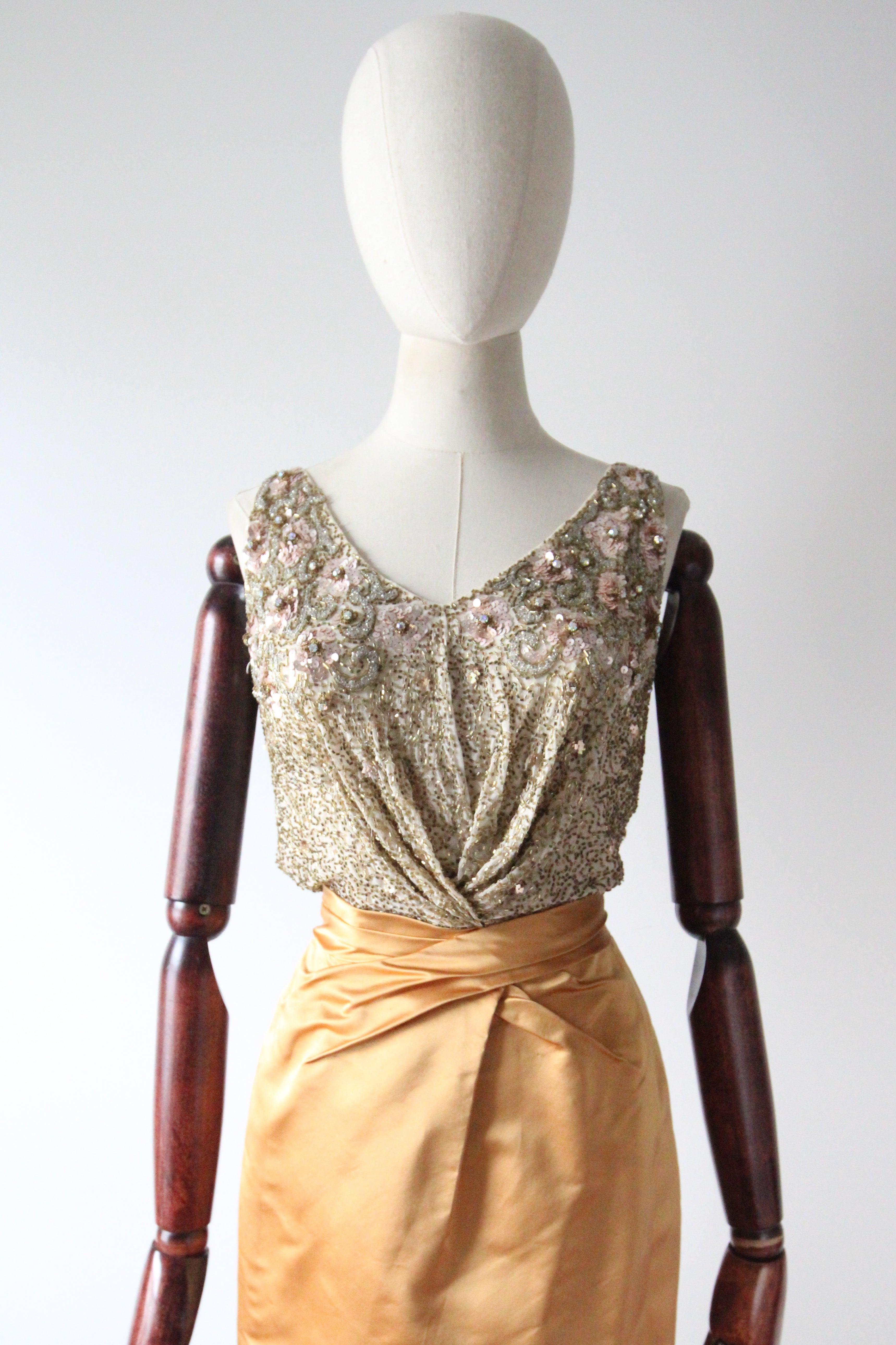 Realizzato in una silhouette classica, questo sontuoso abito anni '50 di Ceil Chapman, in un audace raso dorato, contrastato da un corpetto in seta color crema impreziosito da strascichi di perle di vetro dorate, fiori di seta e paillettes rosa,