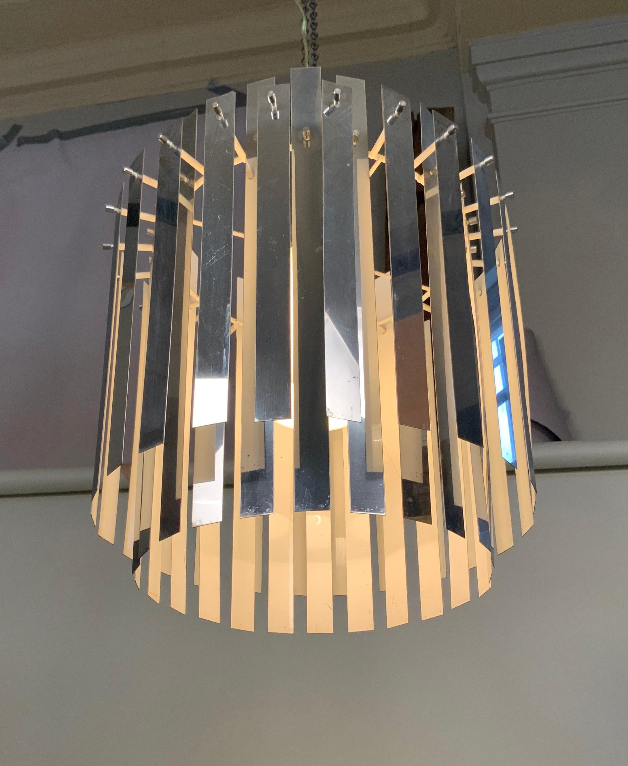 A very interesting vintage 1960s hanging chandelier light fixture, with an iron frame and two rows or chromed steel hanging strips, which create a beautiful effect while concealing the light source, which is also hidden by an opaque glass sleve.