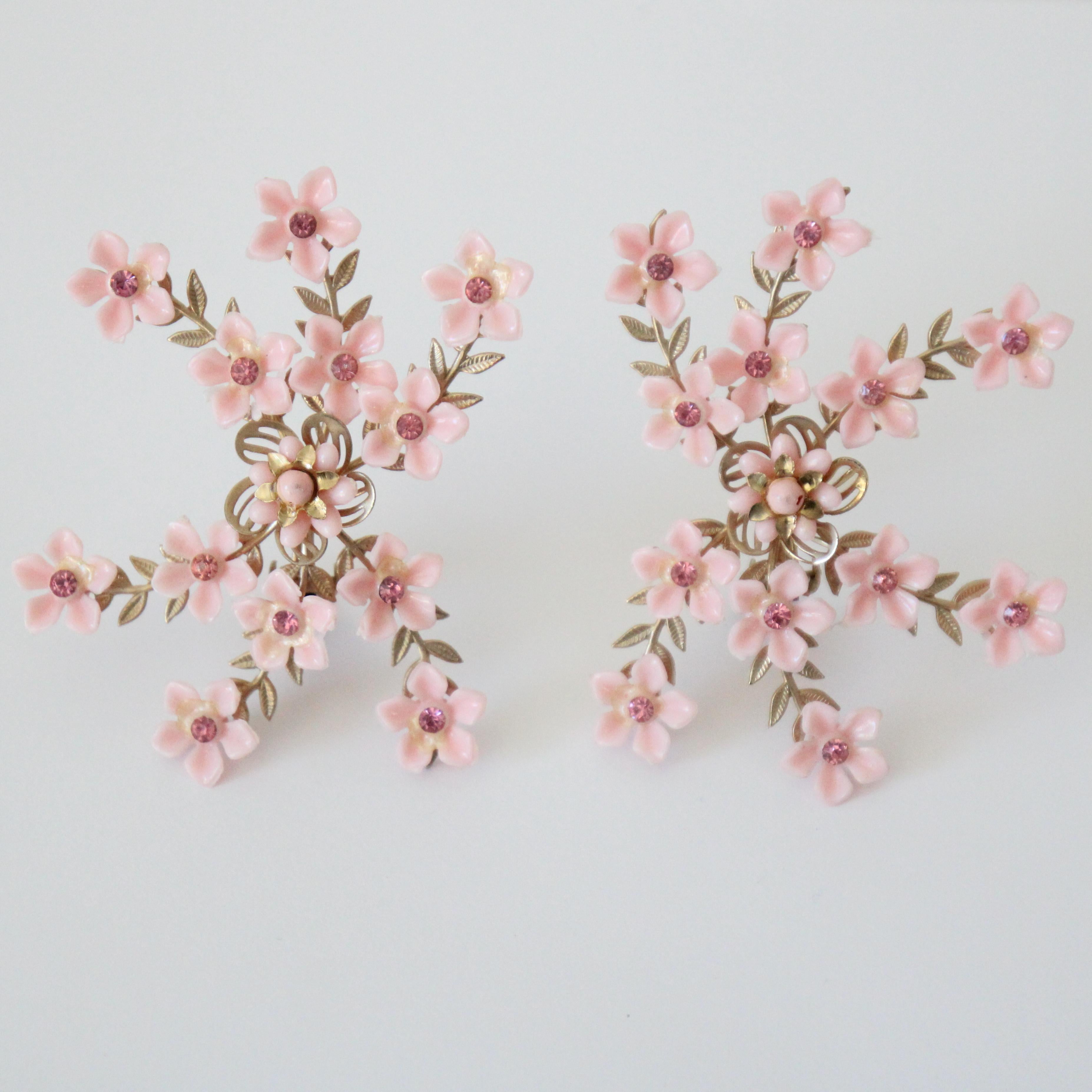 This eye-catching pair of 1950's clip on earrings, on a gold toned metal base made up of 6 separate strands of trailing leaves and pink nylon flowers accented by central pink rhinestone inlays, surrounding a central larger nylon flower contoured by