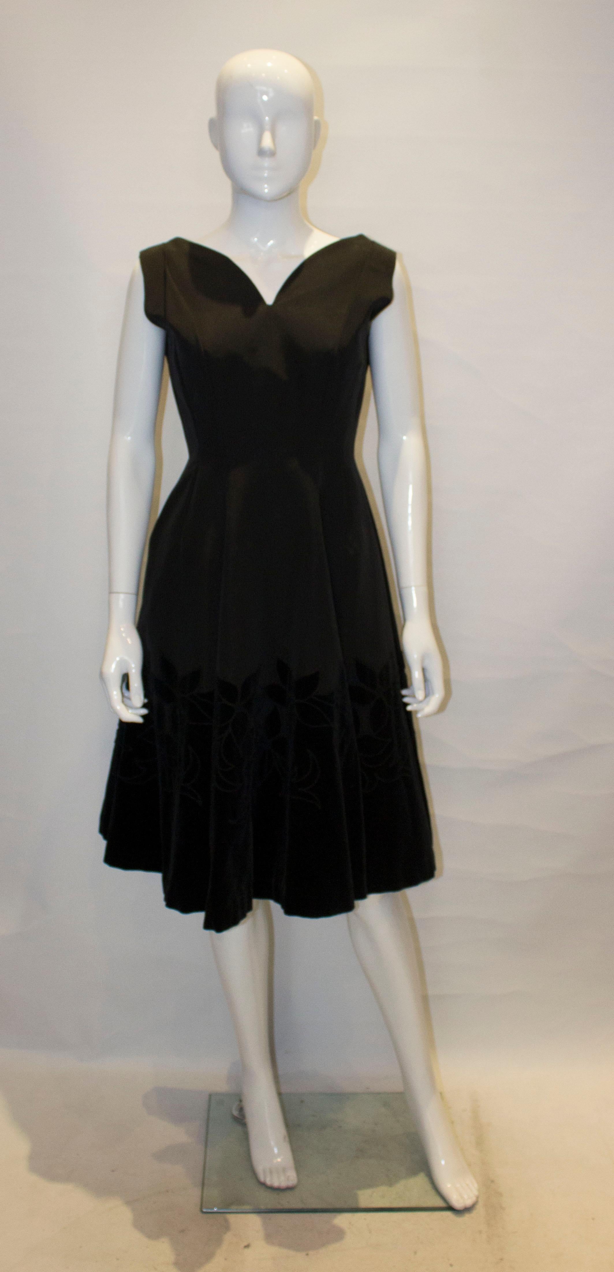 A head turning cocktail dress from the 1950s. The dress has a deep v neckline and backline. with a flared skirt and wonderful velvet flowers and detail on the hem.