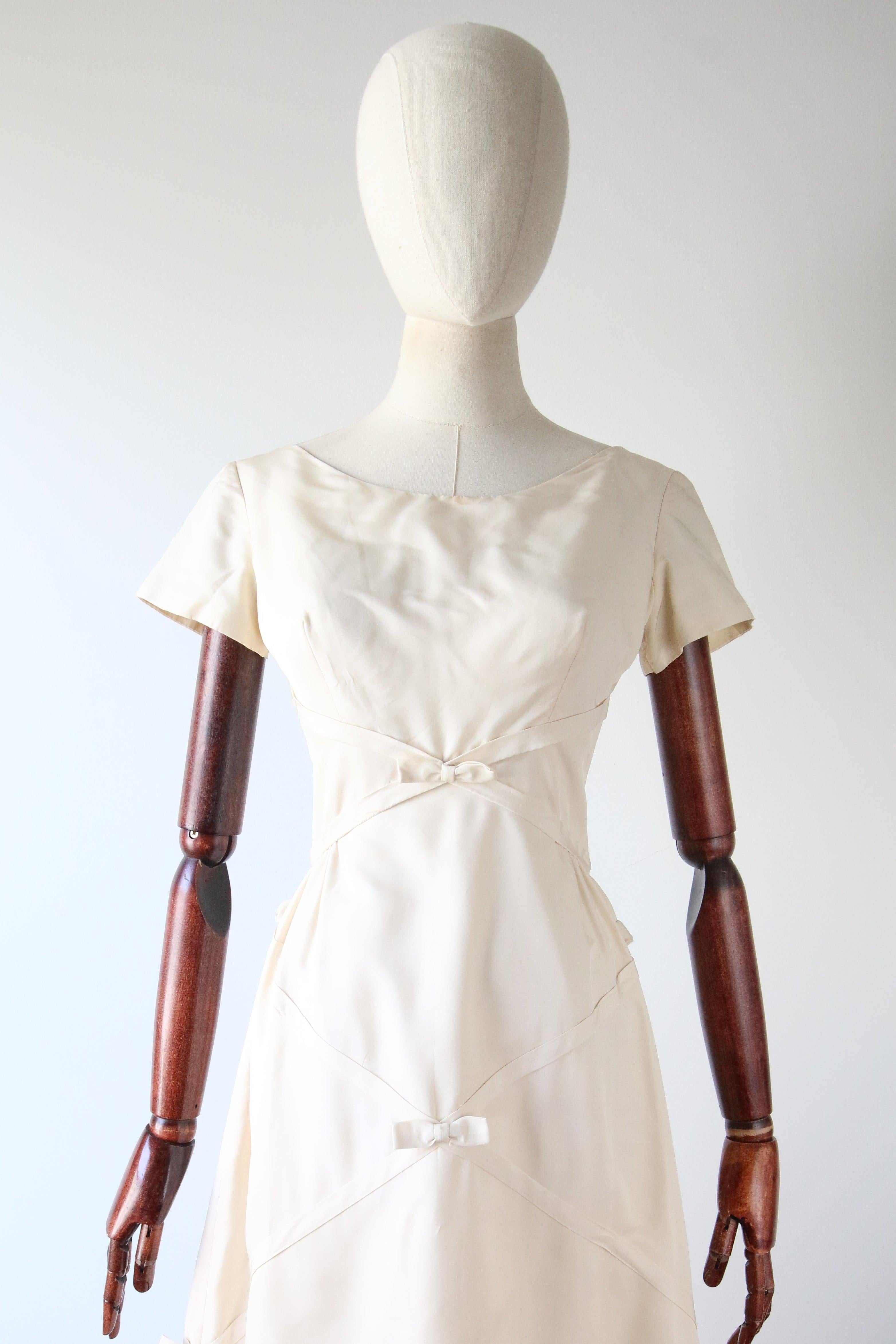 Cette robe de soirée crème des années 1950 à couper le souffle, rehaussée d'un motif de nœuds et de rubans et terminée par les boutons les plus incroyables le long du dos de la robe, est un classique intemporel pour votre collection vintage.