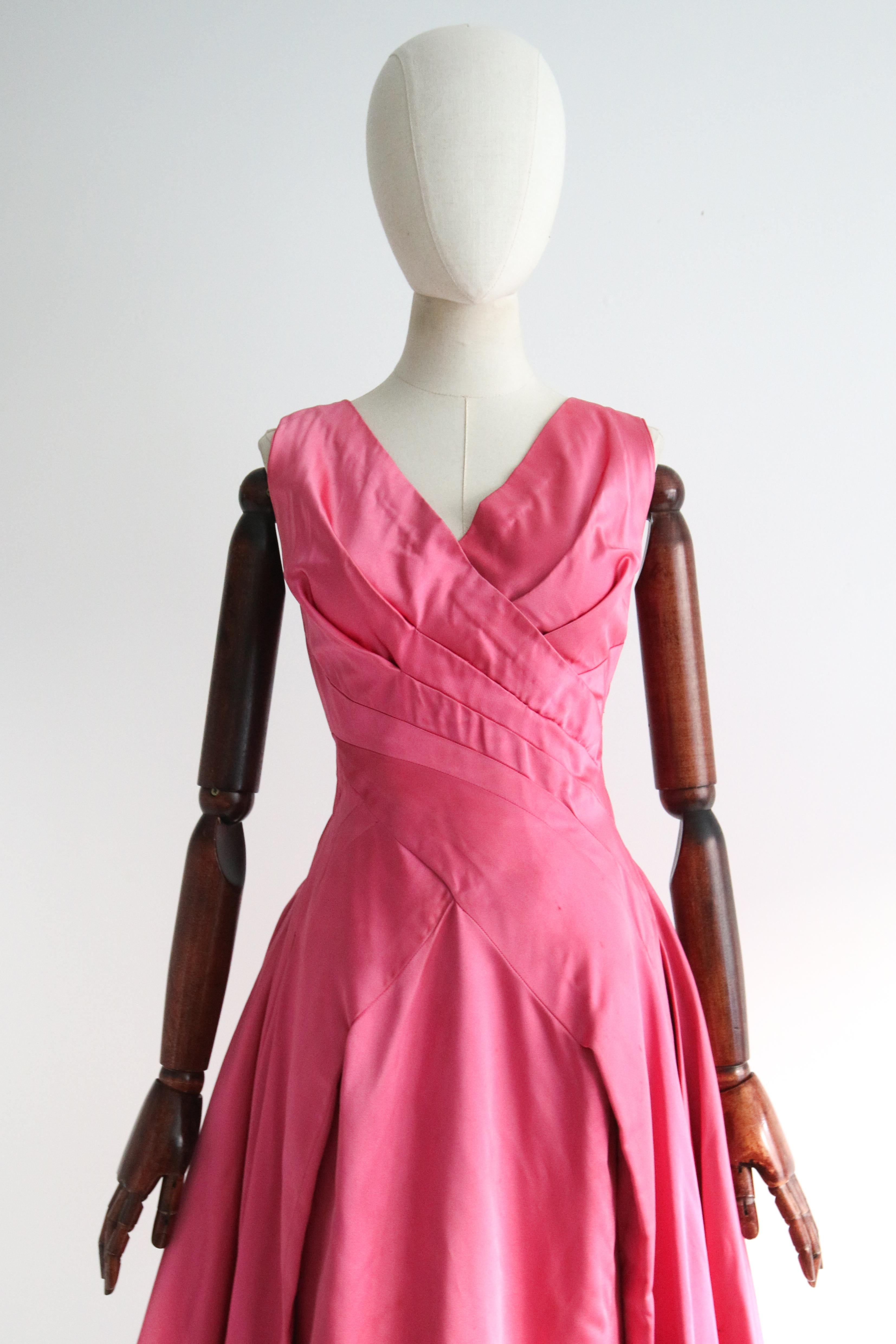 A true beauty to behold. This original 1950's duchess satin dress, rendered in a soft shade of sweet pink and accented by the most divine pleat work, is a timeless beauty to behold and a must have in your vintage collection. 

The V shaped cross
