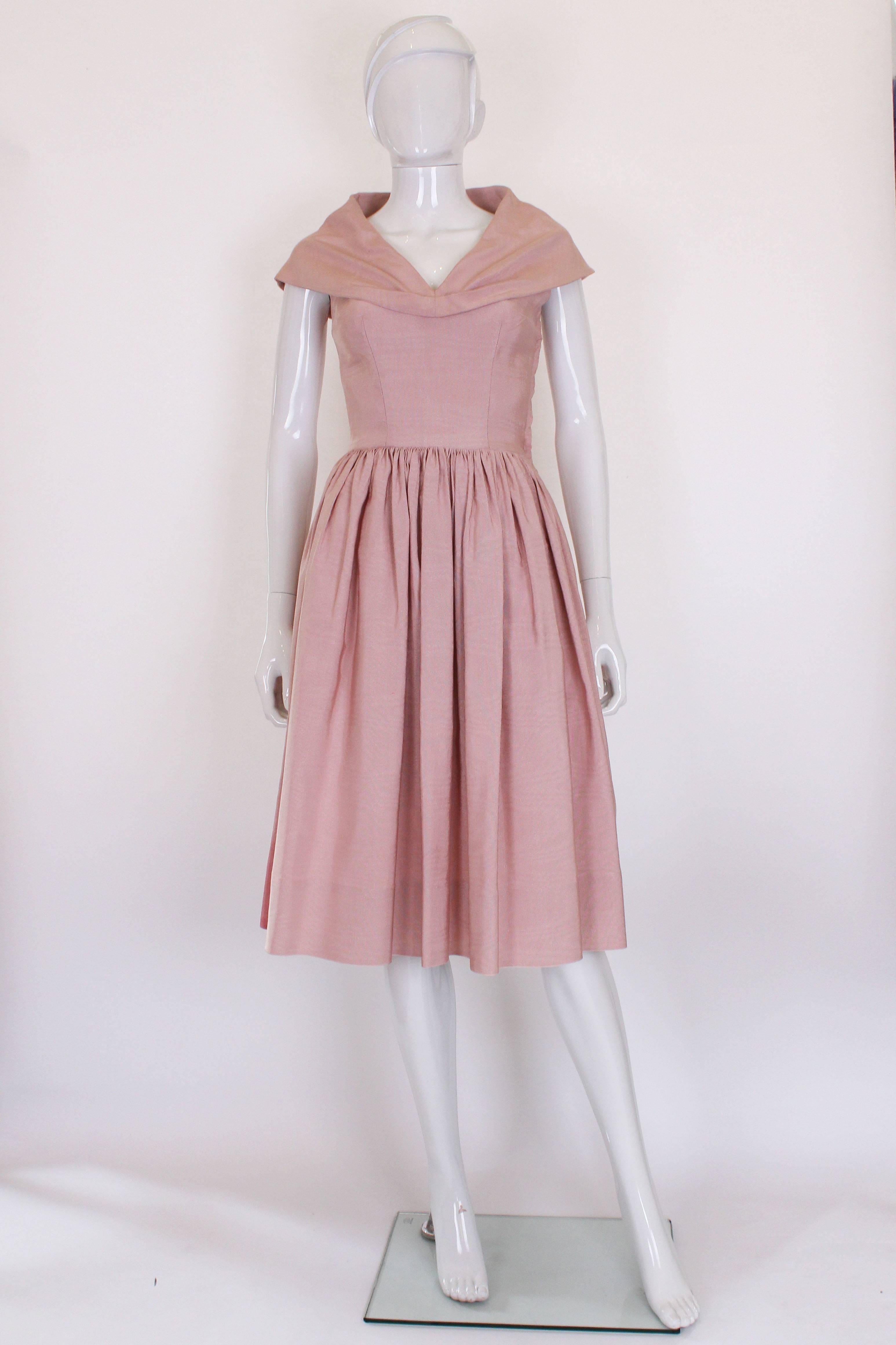 This is a stunning 1950s in a soft dusty pink. The fabric is a ribbed, structured silk that helps to shape the dress. The skirt is densely gathered around the waist so  the skirt has lots of volume. The top is very fitted and has a large shawl style