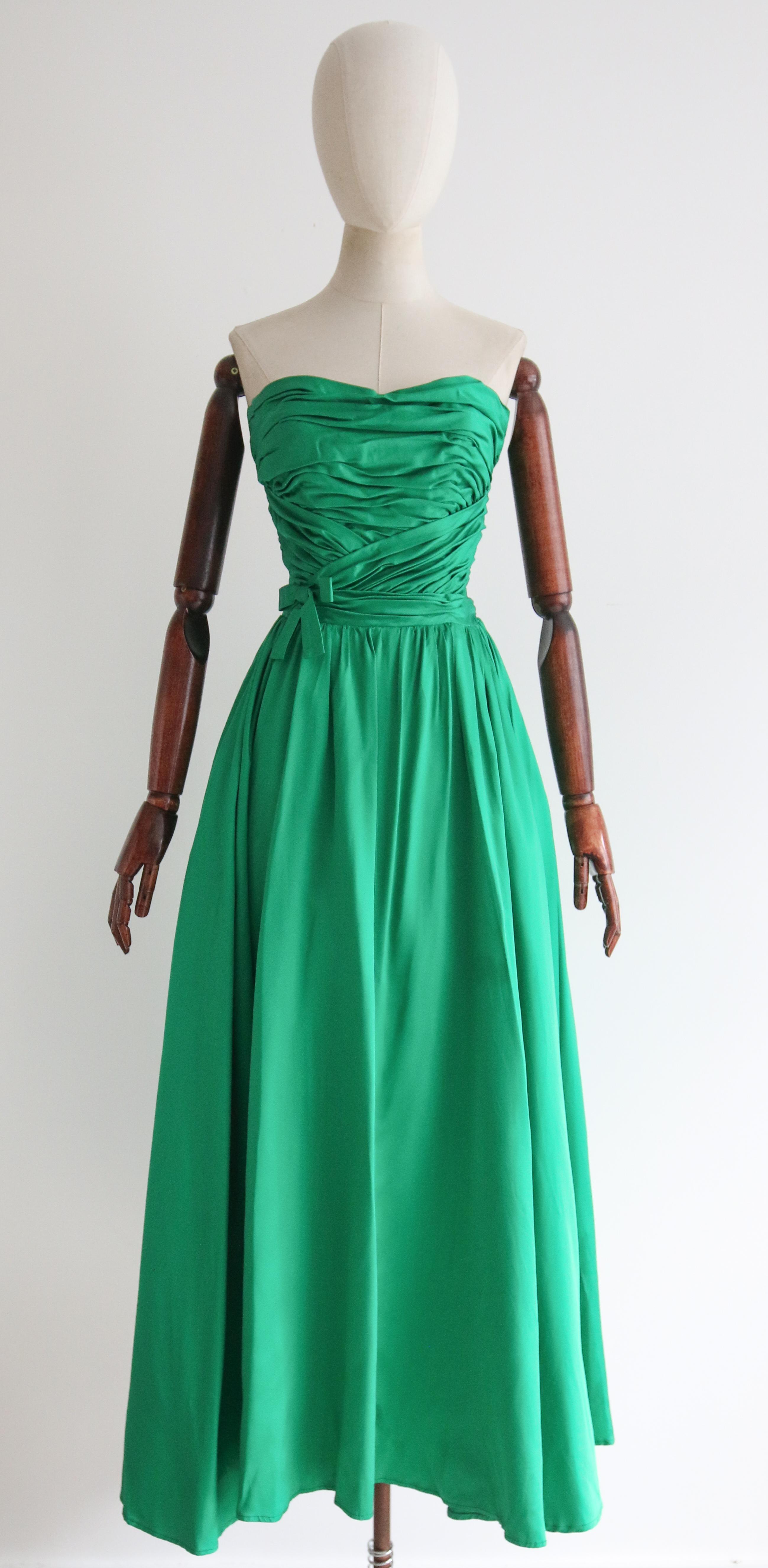 Questo abito mozzafiato in raso duchesse degli anni '50, nella più accattivante tonalità di verde smeraldo, arricchito da pieghe arricciate e da un fiocco decorativo, è il pezzo perfetto per un'occasione speciale. 

La scollatura senza spalline