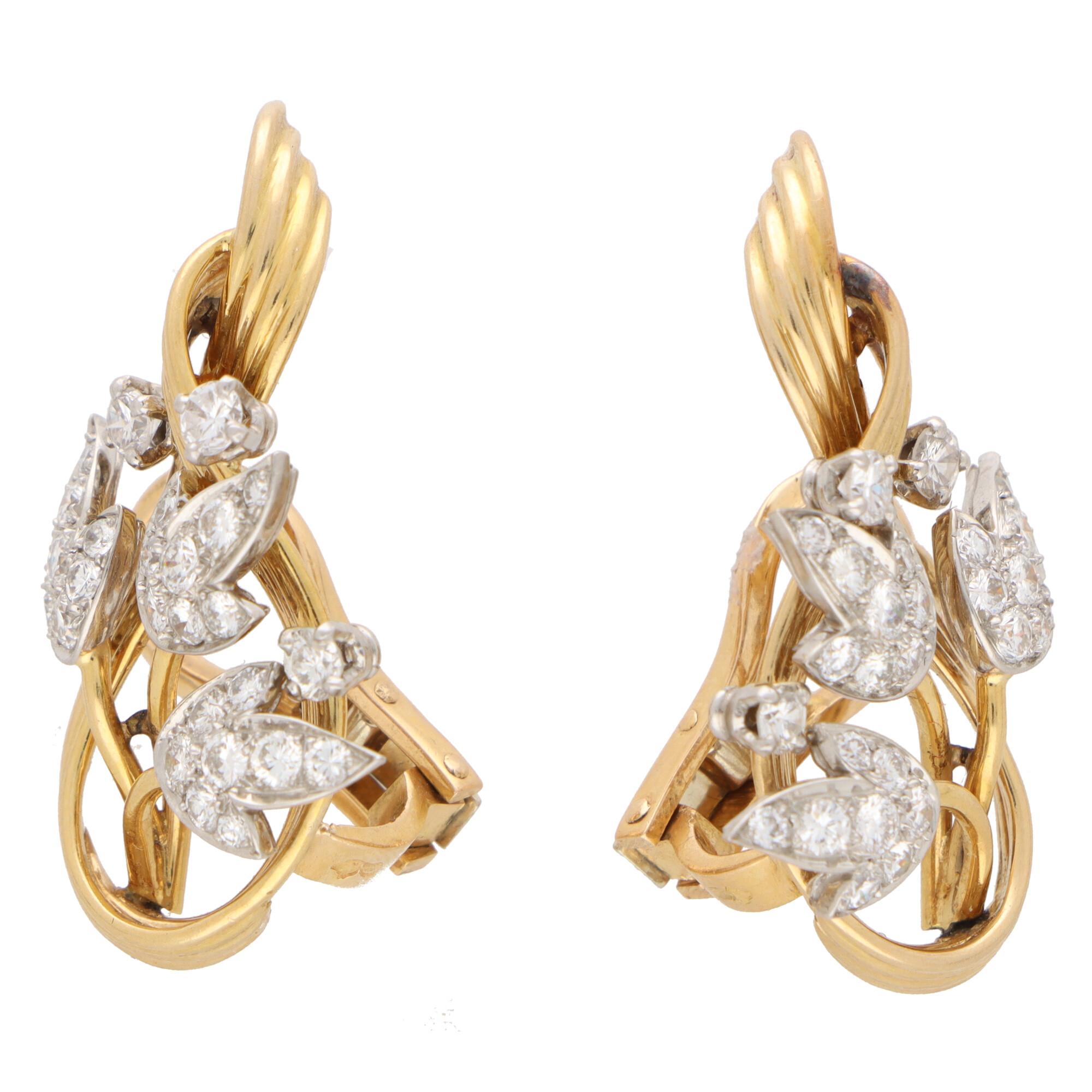 A beautiful pair of floral spray diamond clip on earrings set in 18k yellow gold and platinum.

Each earring is composed of a fluted ribbon surmount in yellow gold, accented with a spray of three flowers blooming inside. Each flower is composed of a