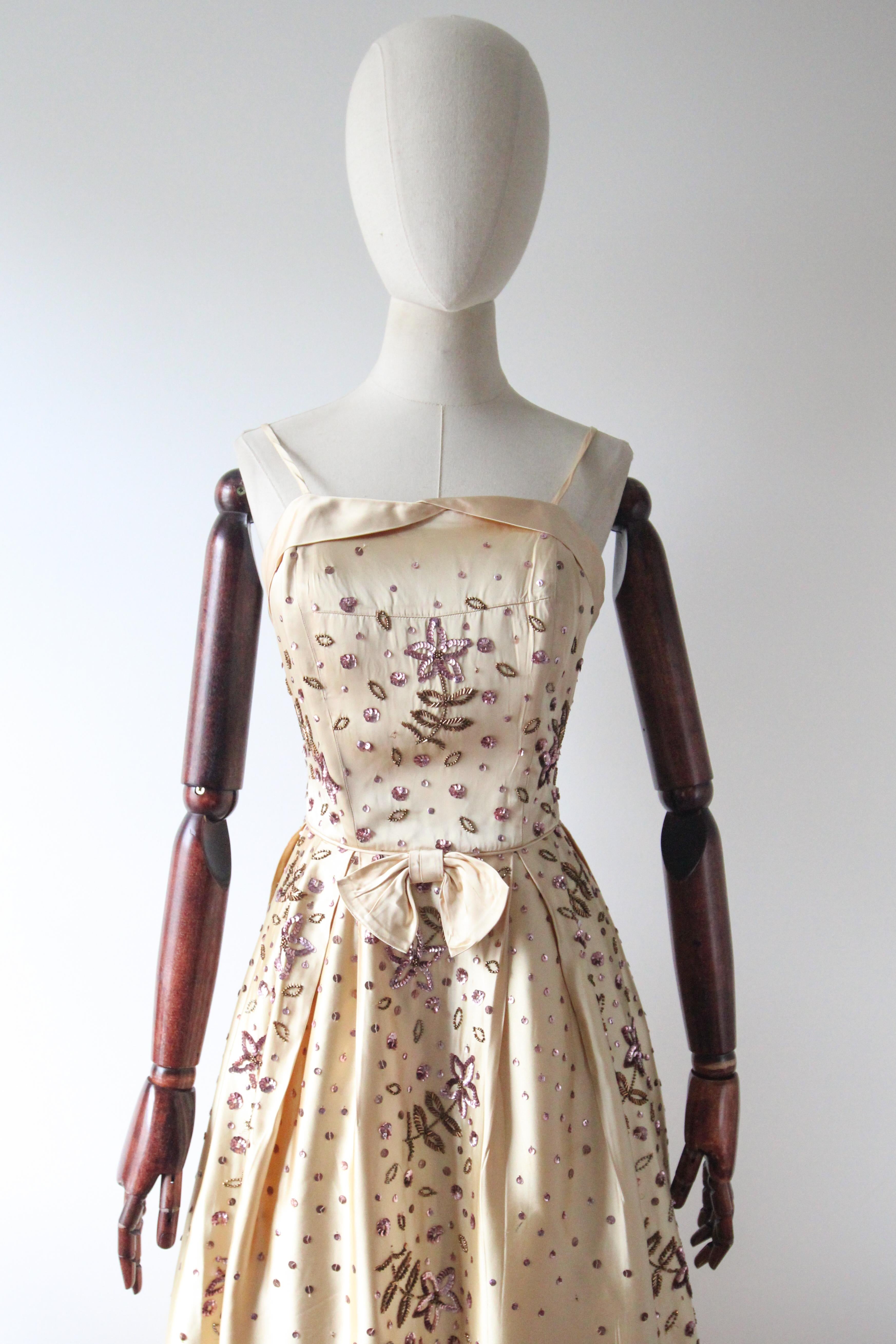 A breathtaking dress, rendered in a sumptuous gold toned yellow satin, embellished with trailing lilac sequins and bronze coloured glass beads in a floral pattern, is the perfect piece for your cocktail wardrobe.

Her thin satin shoulder straps