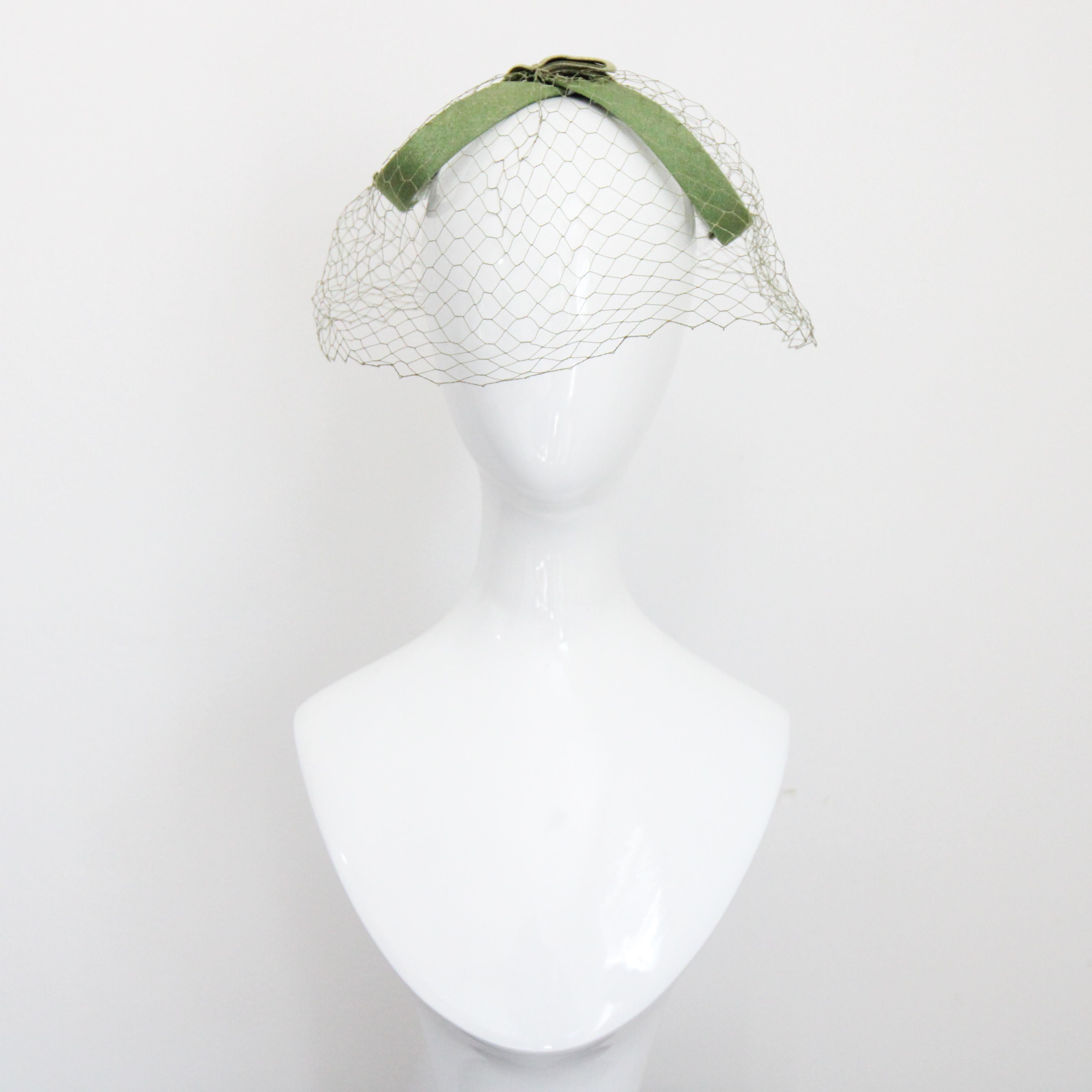 Cet adorable chapeau vert forêt des années 1950, réalisé en rayonne verte texturée, doublé intérieurement d'entoilage, en forme de 8, est une pièce rare. La forme sculpturale est dotée d'un voile extérieur vert en forme de cage à oiseaux, qui se