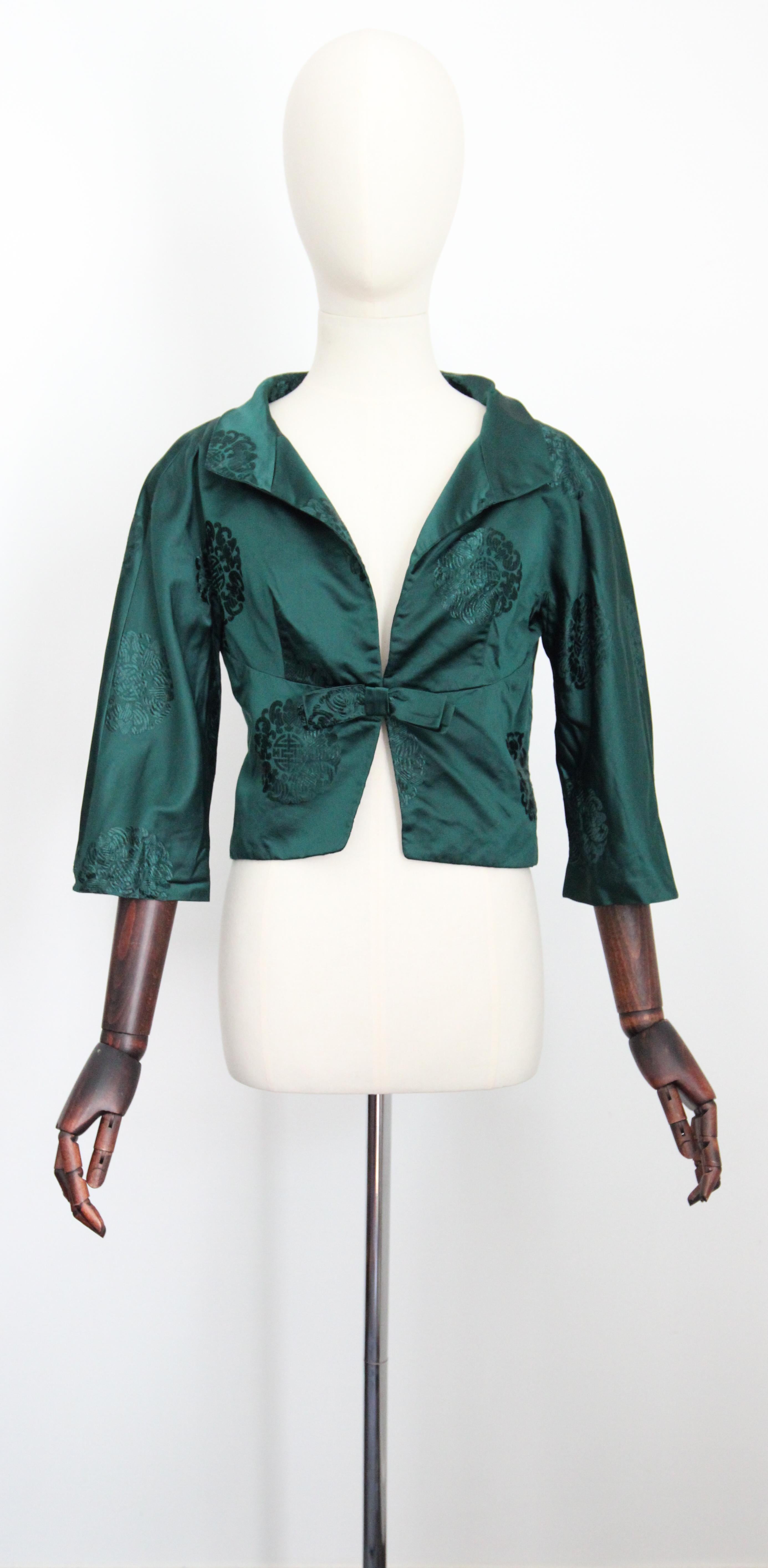 Realizzata nella più sontuosa tonalità di raso verde Sacramento, con un motivo broccato a medaglioni, questa giacca originale degli anni '50 è proprio il pezzo da aggiungere alla tua collezione vintage. 

La profonda scollatura a V è incorniciata da