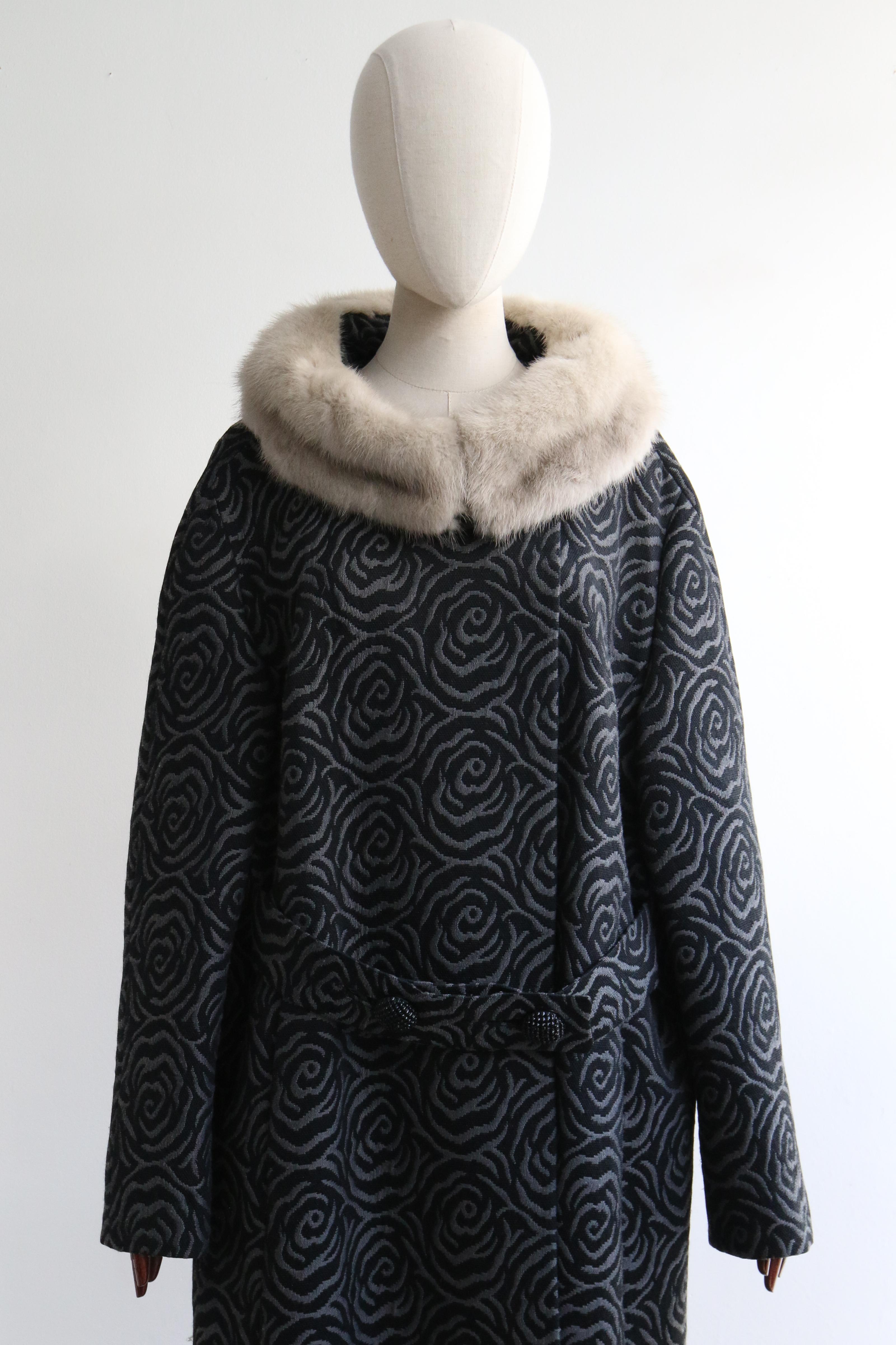 This wonderful 1950's coat, in a grey and black brocade pattern of swirling roses, accented by a silver mink collar is the perfect addition to your seasonal wardrobe.  

The neckline of the coat is framed by a wide grey toned mink full collar that