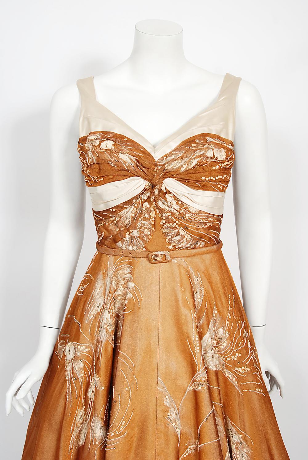 In this gorgeous 1950's hand-painted shimmering copper gown, the detailed construction and meticulous attention to detail are comparable to what you will find in modern couture. This captivating garment is fashioned from sparkling hand-beaded copper