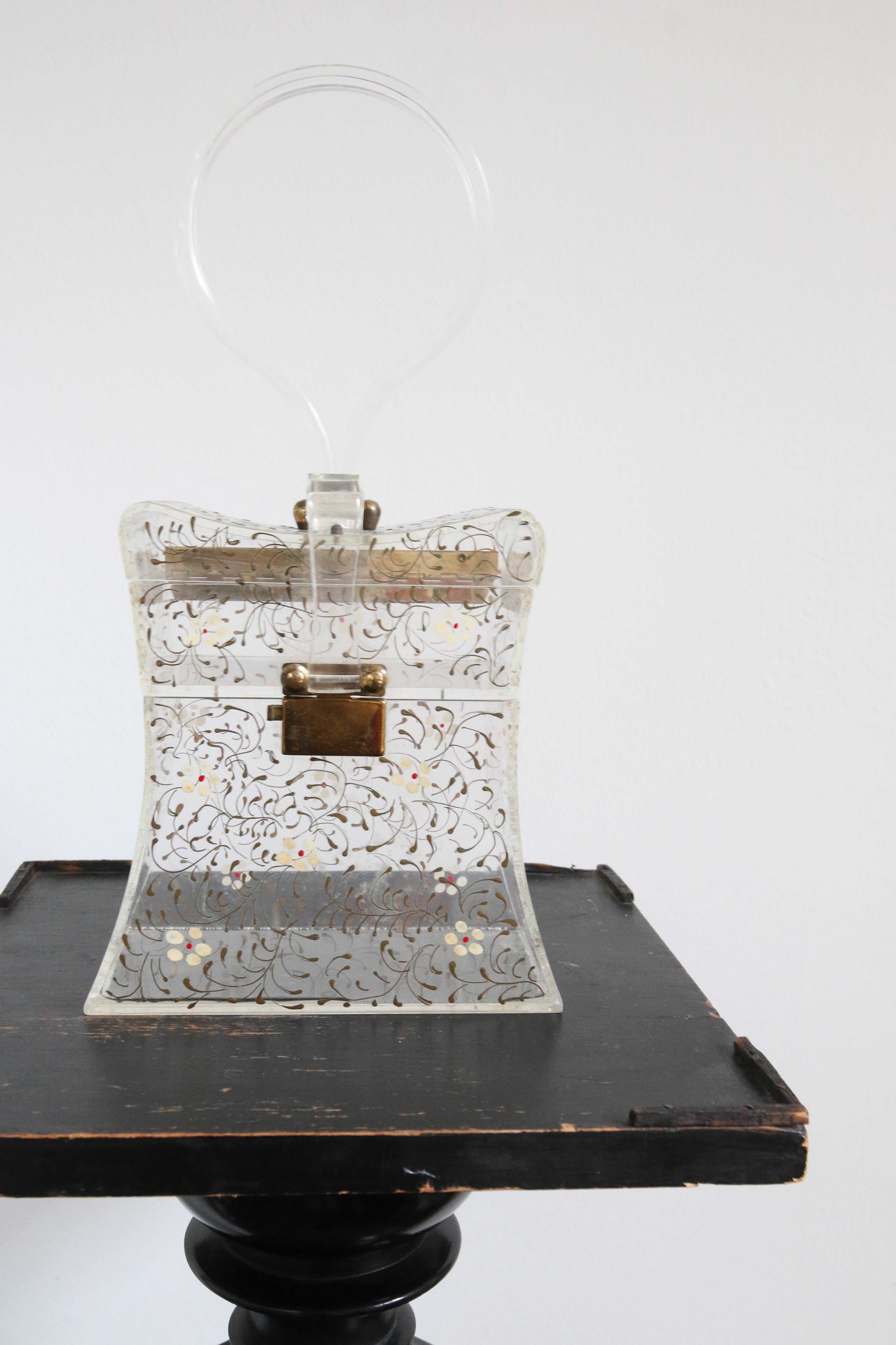 A marvel to behold, this original 1950's clear lucite box bag, accented by hand painted flowers surrounded by trailing green florals, is just the statement piece to add to your vintage collection.
The wonderful size and elegant Pagoda shape of the