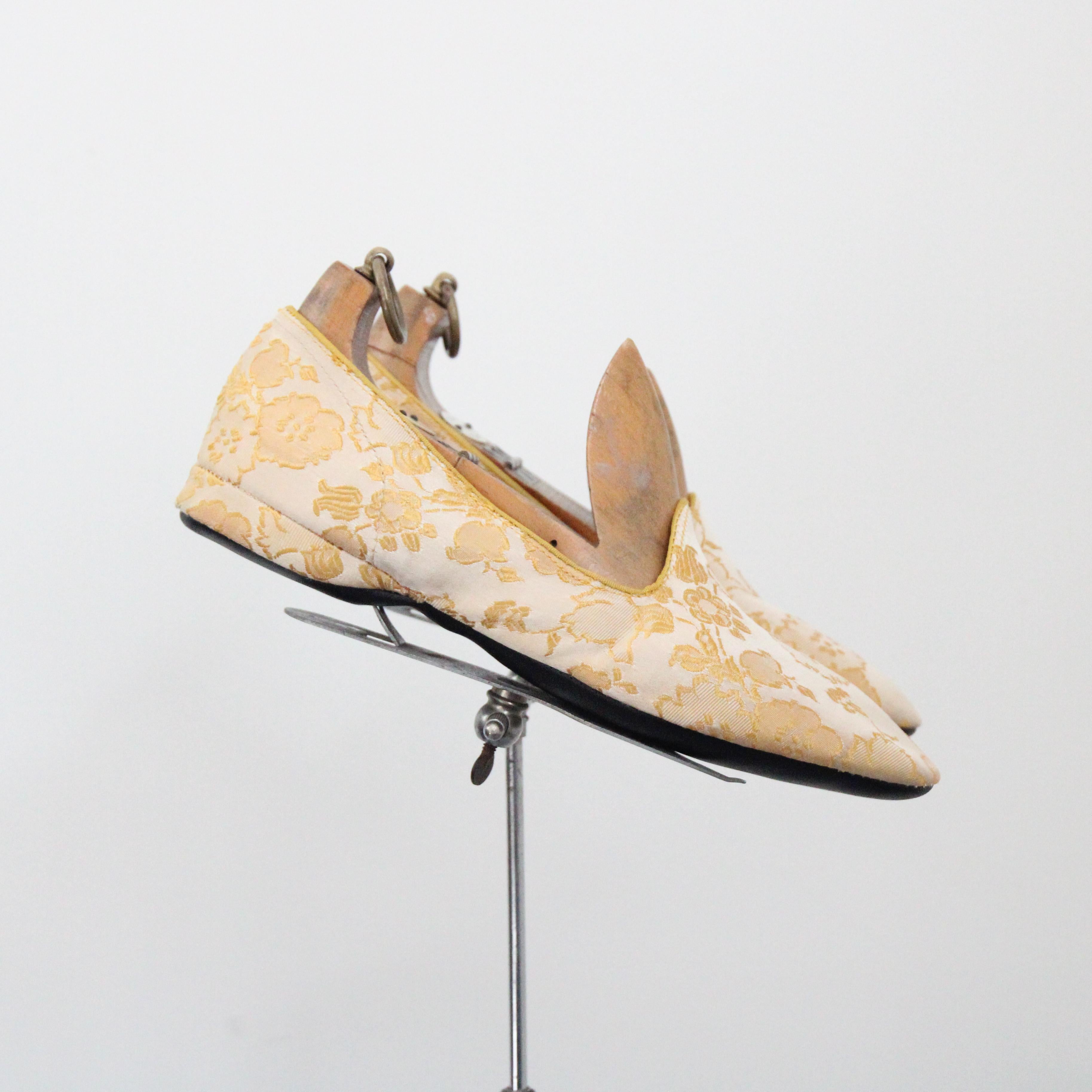 Estas encantadoras zapatillas brocadas en crema de mantequilla de los años 50, con un floreciente estampado floral, son el par perfecto para mantenerte elegante dentro de casa. Este elegante diseño de mocasín presenta un ribete dorado en los bordes