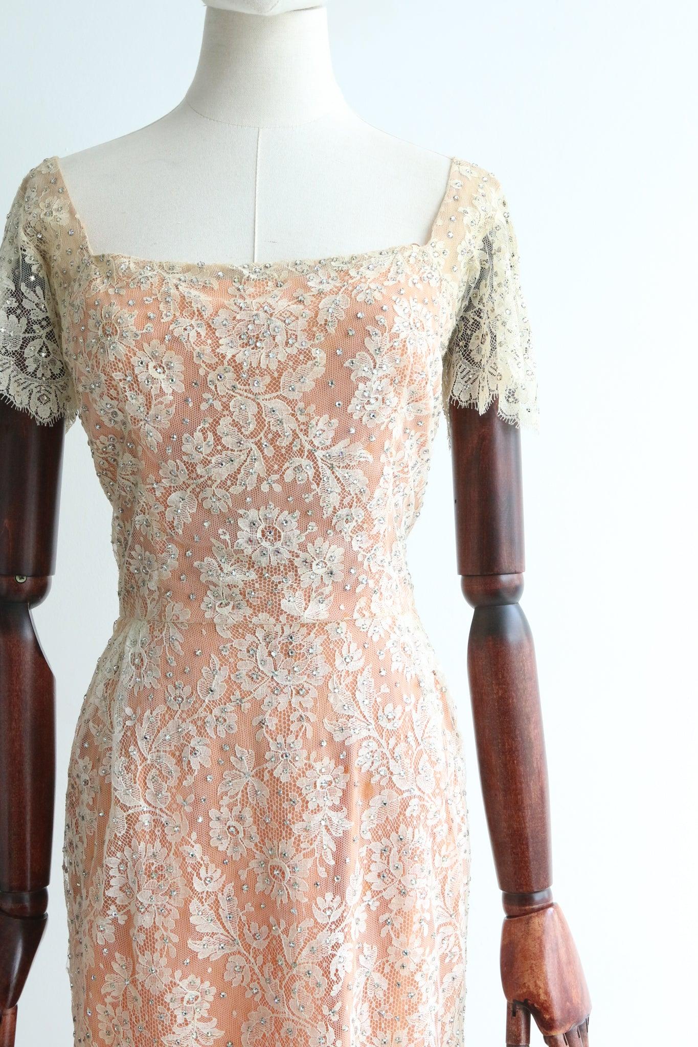 Dieses prächtige Kleid aus Chantilly-Spitze und Seide aus den 1950er Jahren mit cremefarbenem Spitzen- und apricotfarbenem Seidenfutter, akzentuiert durch silberne Strasssteine, ist ein seltenes Stück, das man sehen kann, und ein Statement für Ihre