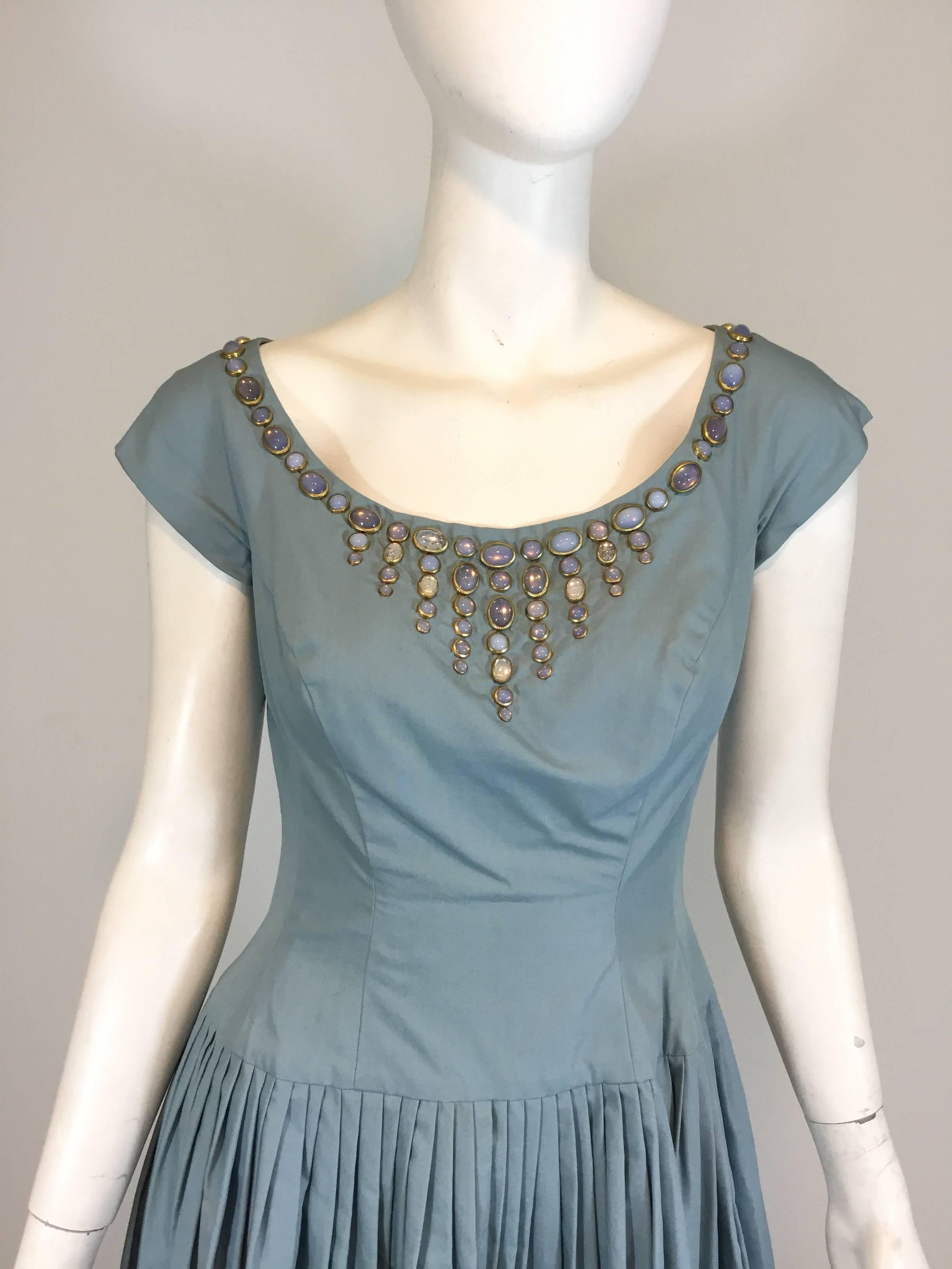 I. Magnin 1950's Vintage dress featured in a robins egg light blue with a faux moonstone jewel-embellished neckline, pintucked skirt, and a back zipper fastening. Jewels are set in goldstone metal and are a cabochon shape. Excellent
