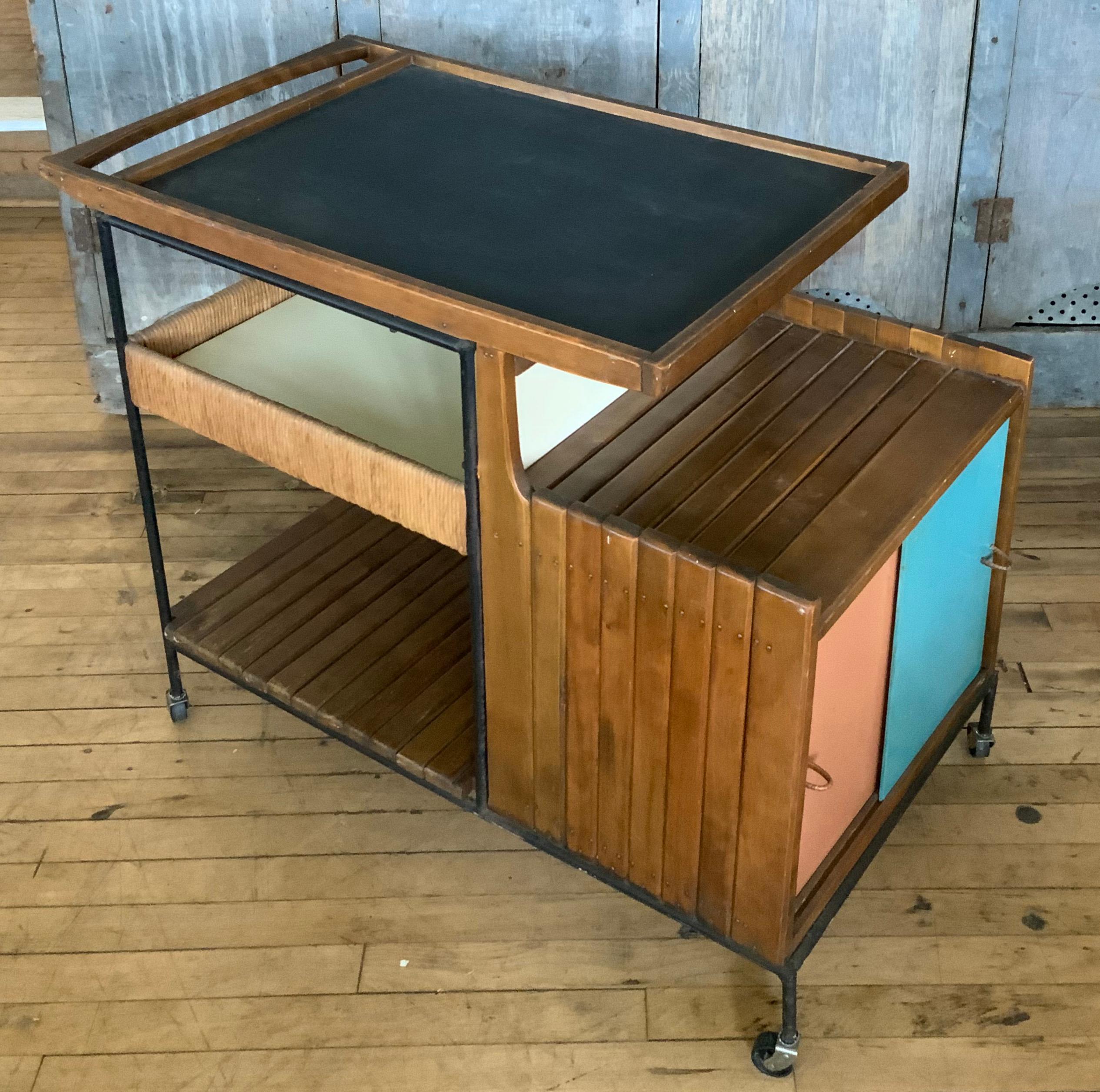 a very handsome and classic mid century rolling bar cart by Arthur Umanoff. the cart has a wrought iron frame, with maple case and one section wrapped in rope. the lower cabinet has sliding doors in their original colored panels. beautiful