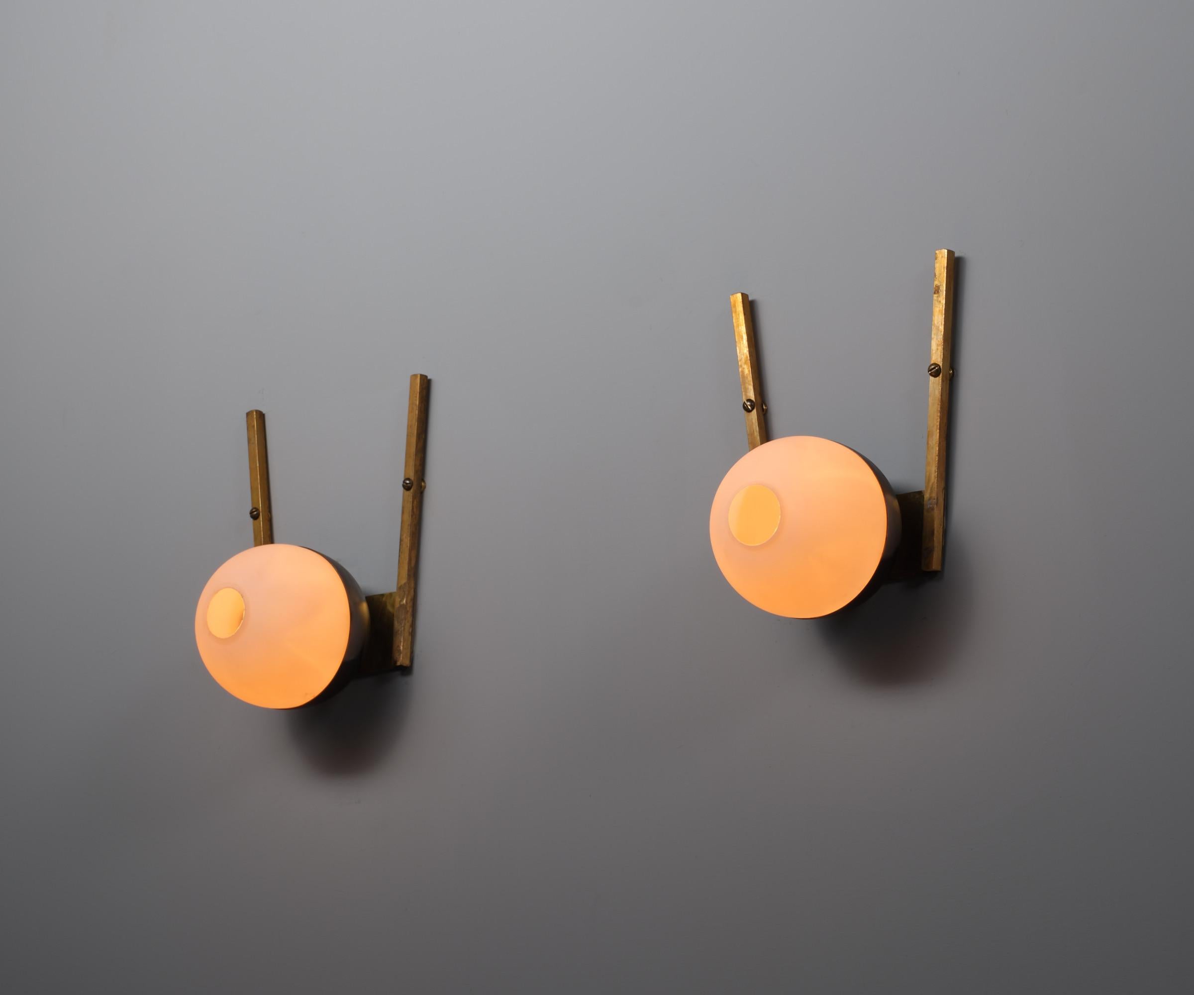 Presented here is a pair of Italian wall sconces from the 1950s, crafted from brass and featuring spherical opal glass shades. The brass arms exhibit a mature patina with subtle signs of oxidation, characteristic of genuine vintage pieces, while the