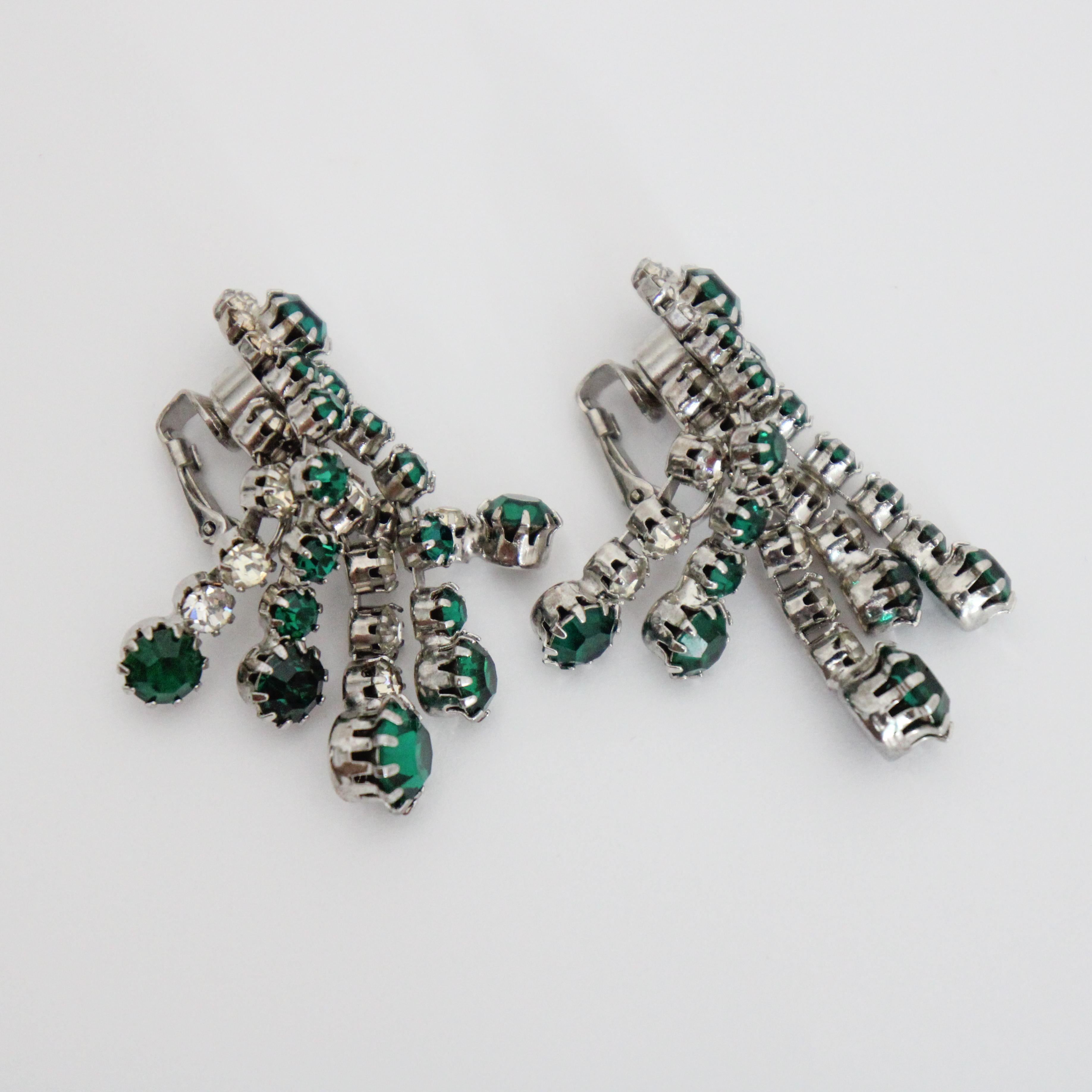 Dieses Paar Ohrclips von Kramer aus den 1950er Jahren ist mit zwei Strasssträngen aus smaragdgrünen und silbernen Steinen verziert, die in silberfarbenen Metallfassungen gefasst sind und an einem floralen Strassmuster aufgehängt sind. Sie verleihen
