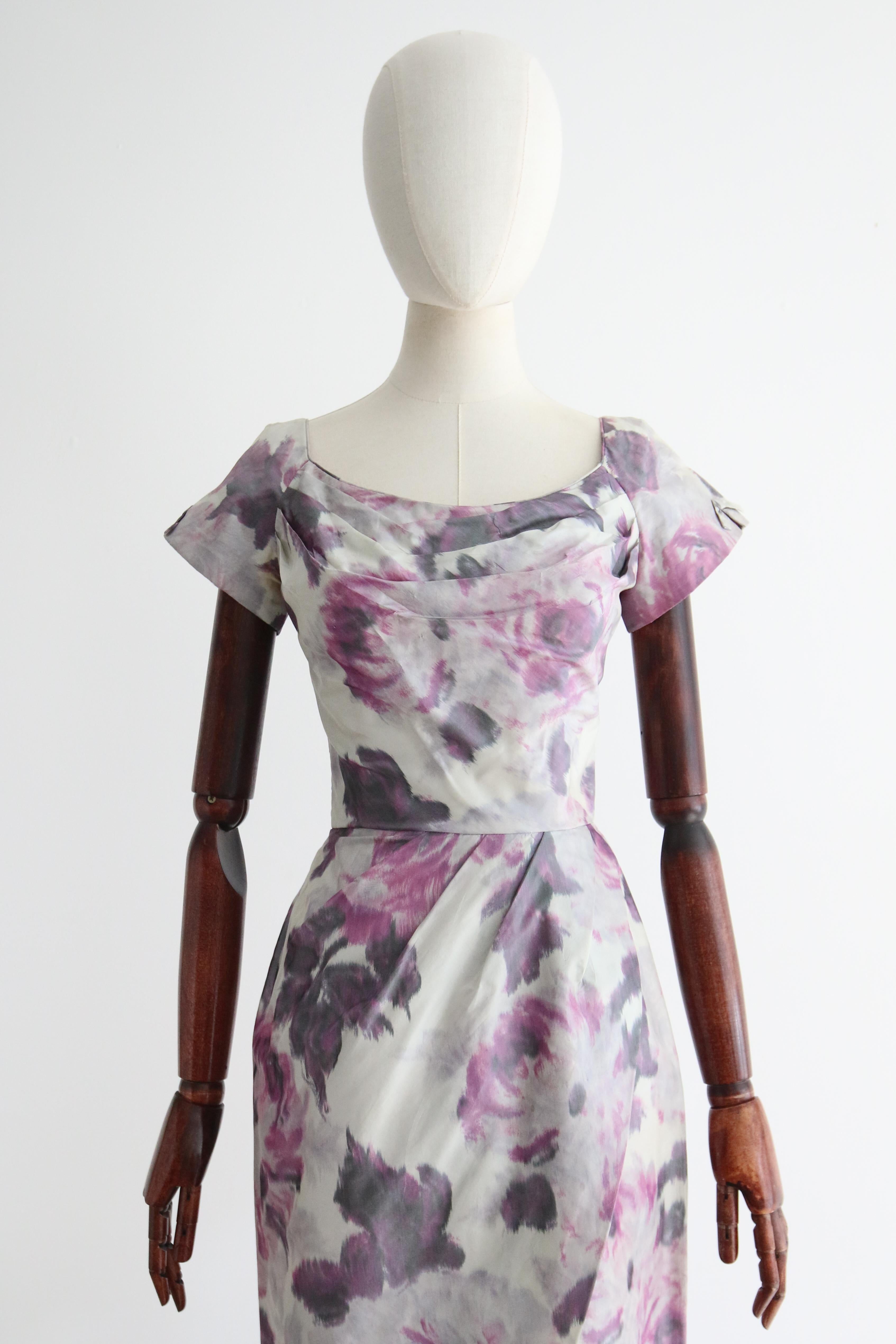 Dieses originelle Kleid aus Wasserseide mit Blumenmuster aus den 1950er Jahren ist in den reizvollsten Fliedertönen auf taubengrauem Hintergrund gehalten und genau das richtige Stück für Ihre Vintage-Sammlung.  

Der runde Ausschnitt des Kleides