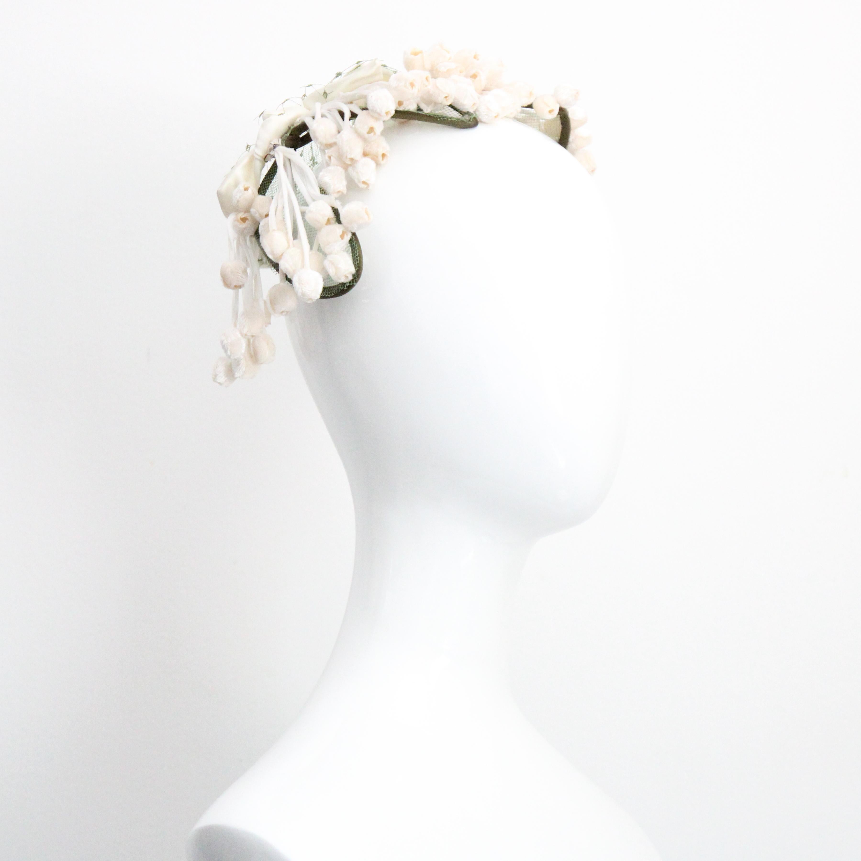 Rendered in the softest shades of cream velvet and rayon satin, with green millinery netting accents and green rayon satin details, this original 1950's vintage hat, decorated with lily of the valley flowers, is the perfect piece to complete your
