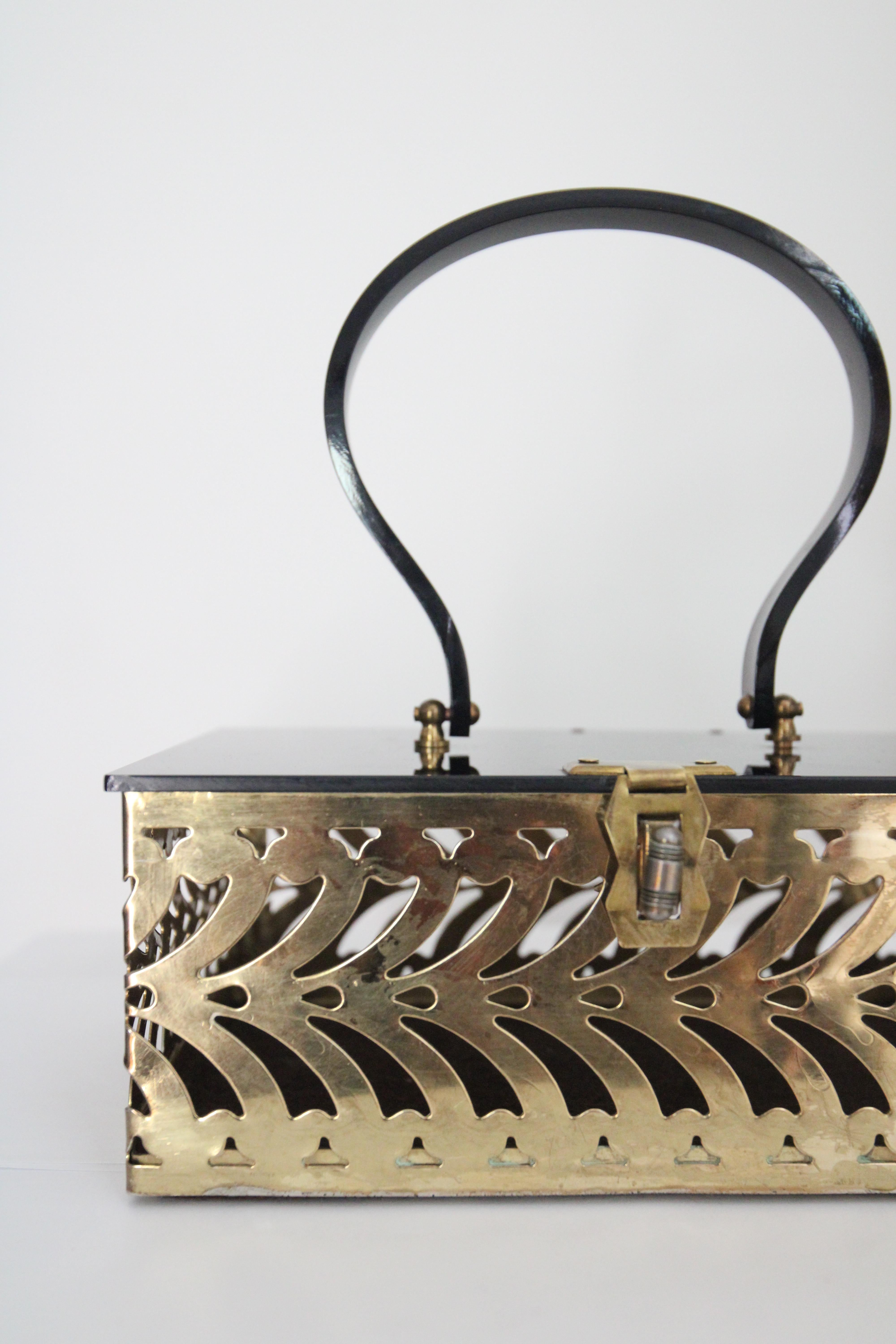This breathtaking 1950's lucite and gold toned metal box bag, in the most interesting cut out design, is the perfect accessory for any vintage lover.

The rectangle shape of the bag showcases a gold toned cut out brass metal decorative body in a