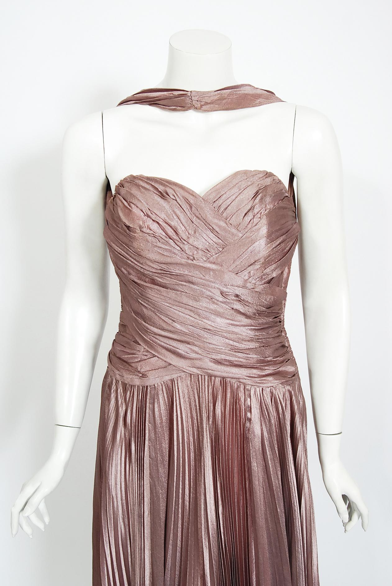 Une magnifique robe de soirée du milieu du siècle dernier, créée par la maison de couture londonienne Marjon Couture. Le tissu utilisé est de la plus haute qualité ; une soie doublée d'un mauve léger et chatoyant. Le corsage de cette robe est un