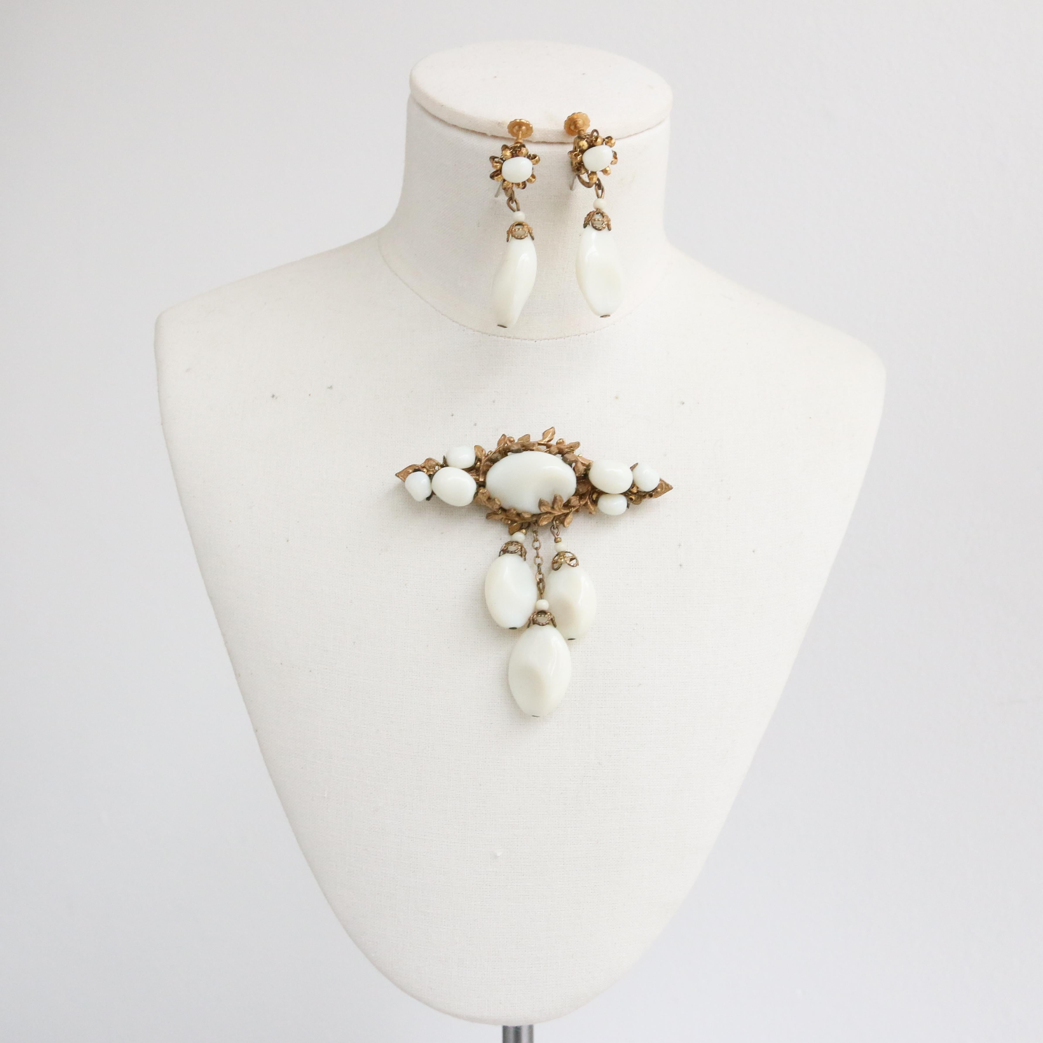 This incredible 1950's Miriam Haskell brooch and earring demi-parure set, made up of statement hand worked milk glass and a leaf filigree design are rare pieces to behold.

The pendent brooch showcases an ornate gold filigree design decorated with