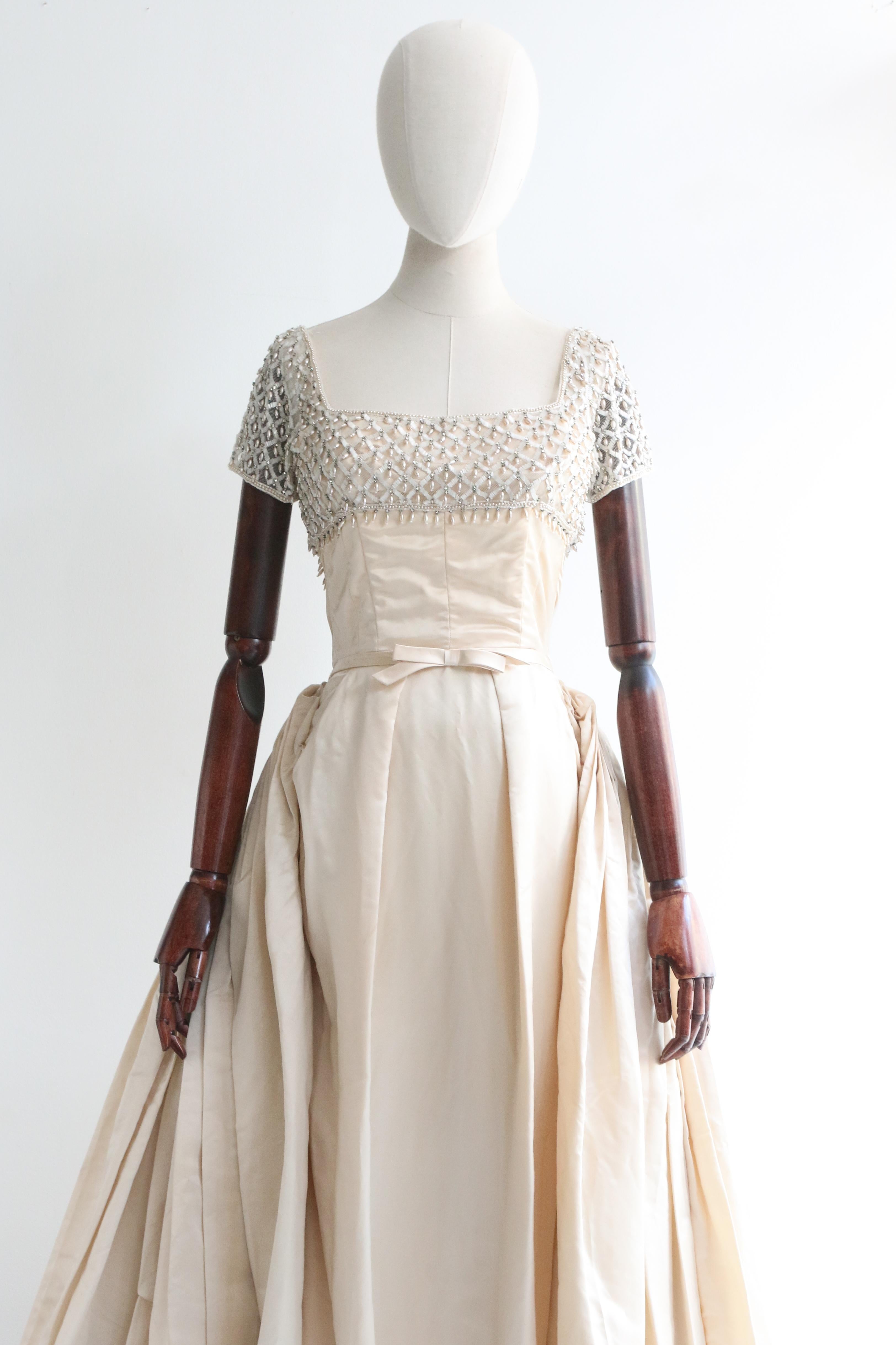 Dieses originale Neymar Couture-Duchess-Satin-Kleid aus den 1950er Jahren in einem prächtigen Cremeton ist ein einmaliges Stück und zeigt wahre Handwerkskunst in seinem Design und seiner Konstruktion. 

Der gerade Ausschnitt ist auf einer Tüllbasis