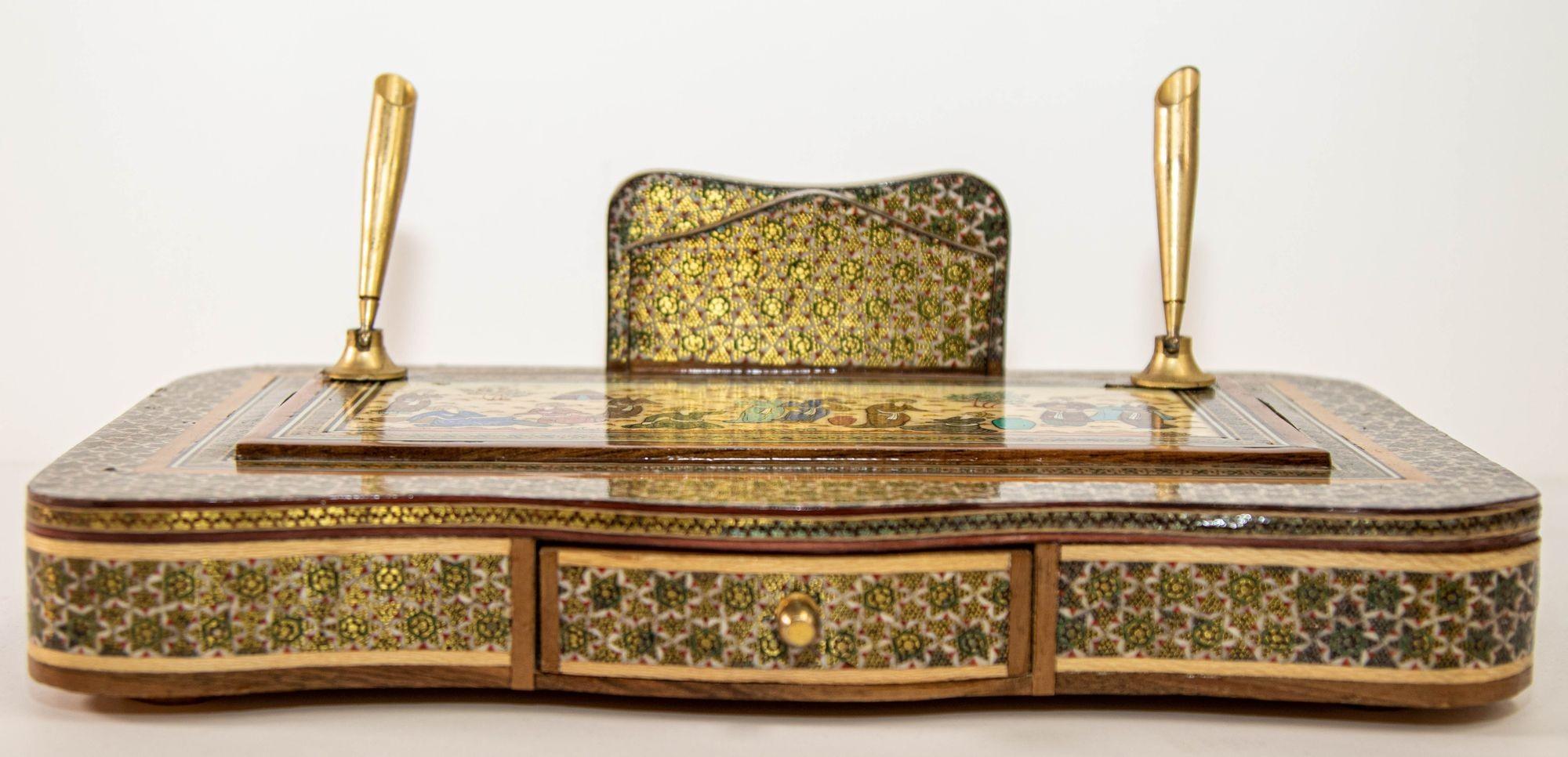 Vintage 1950s Persian Khatam Schreibtisch-Set in Massivholz Mosaik-Inlay mit Messingspitzen Stifthalter.
Der hölzerne Sockel ist mit Khatam bedeckt, und auf der oberen flachen Seite ist eine Miniaturmalerei zu sehen, die junge Menschen, Mädchen und