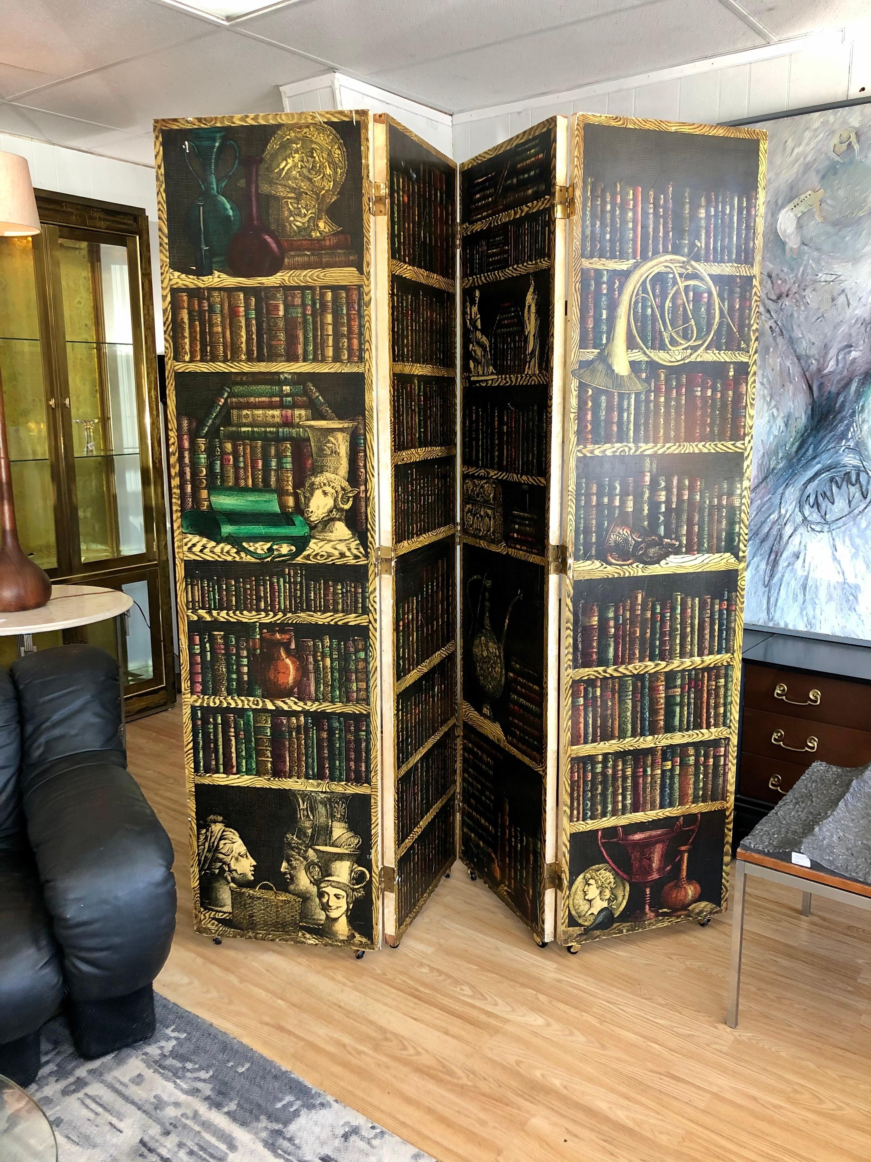 Designed by artist Piero Fornasetti, this four panel folding screen is in overall good condition. Panels depict library filled with books and other objects on shelves and on the reverse a monochromatic scene with busts and drapery. Several scuffs
