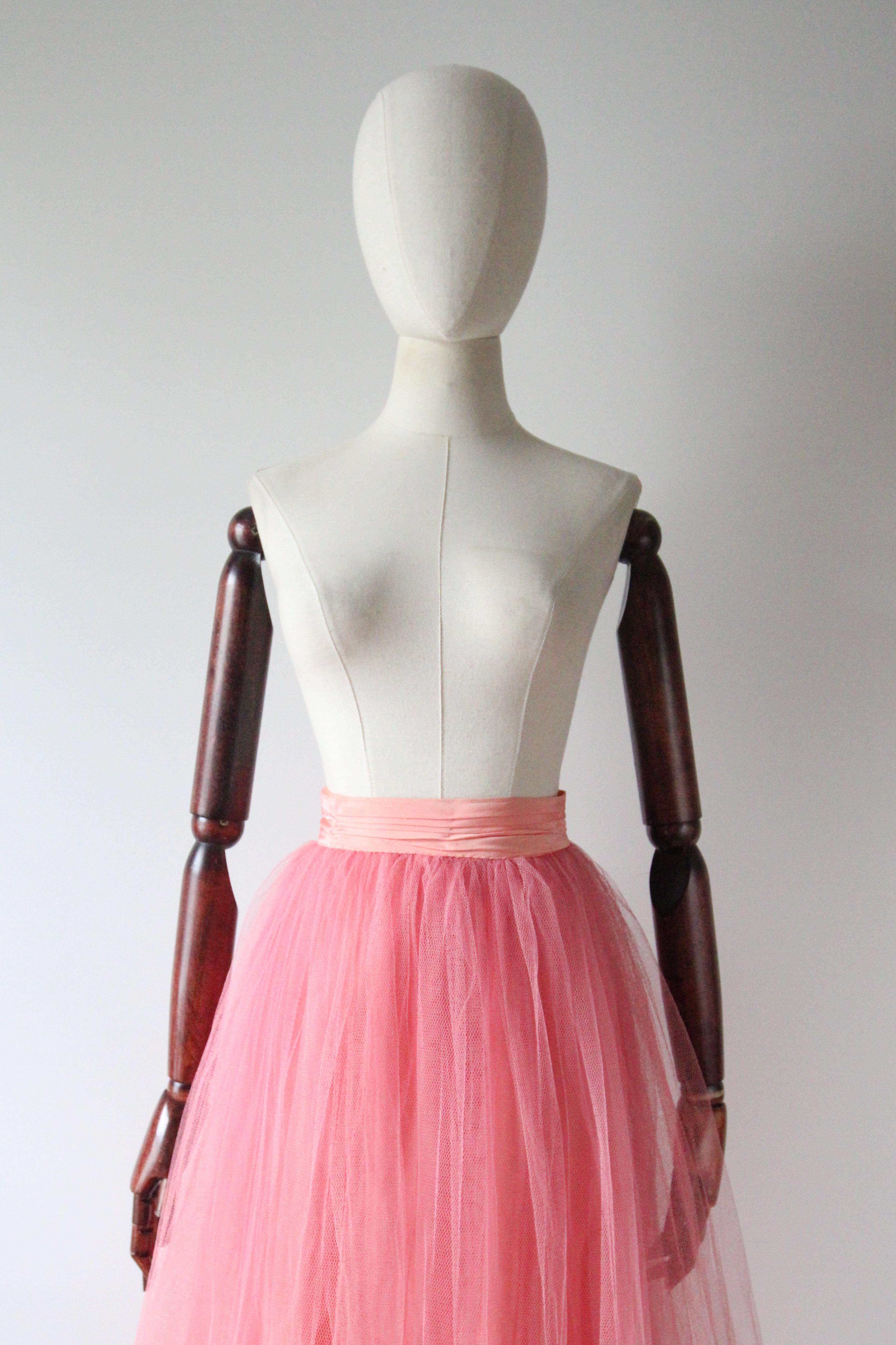 This wonderful 1950's pink tulle petticoat skirt, is the perfect piece to add texture to your vintage wardrobe, or alternatively worn beneath a dress for added volume. 

The fitted and pleated peach rayon waistband, draws in along the back of the