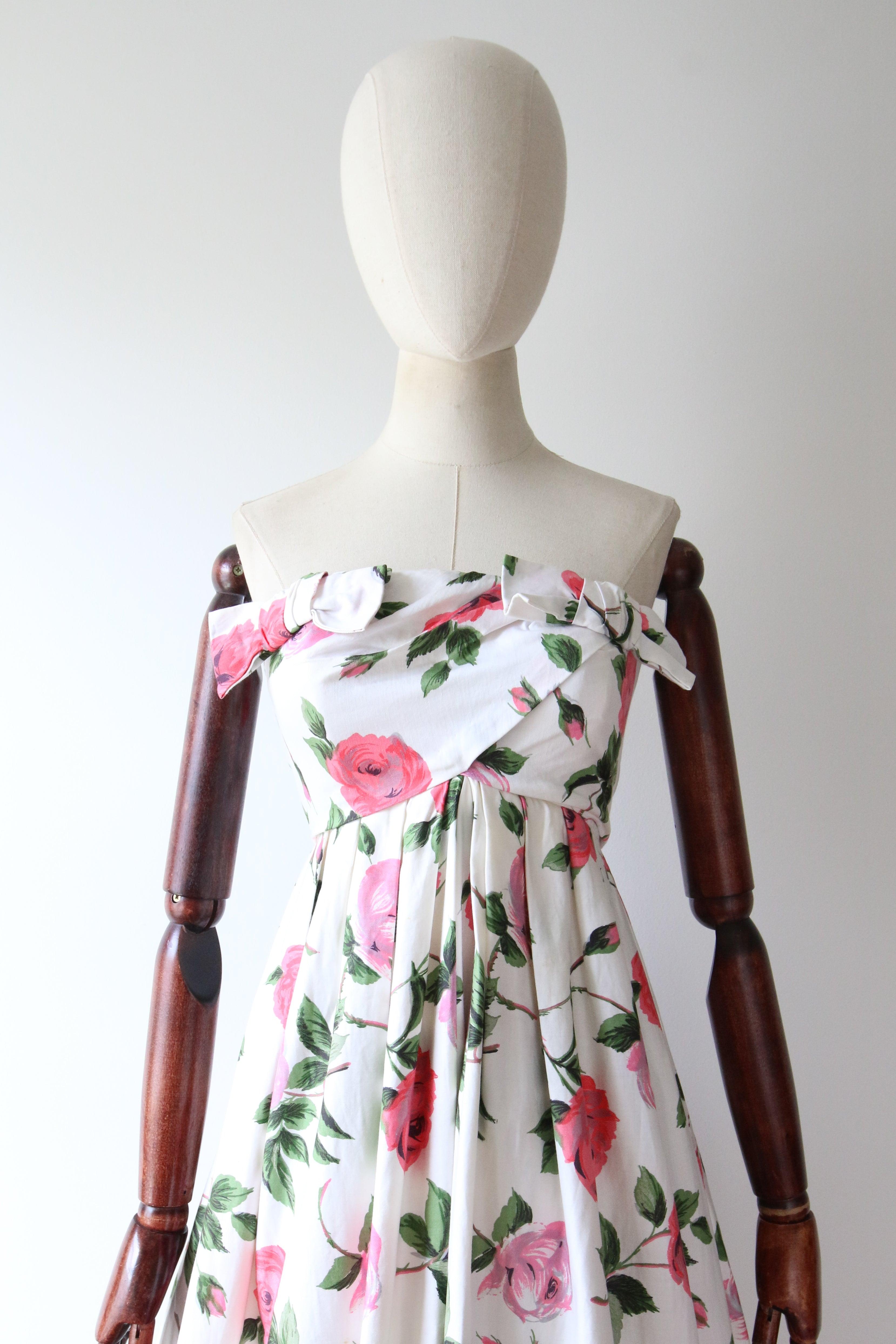This spectacular 1950's dress, rendered in a pink floral rose print with fresh green leaves and stems, set against a white background, is just the piece to welcome to your seasonal wardrobe. 

The strapless neckline of the dress, is set off by a