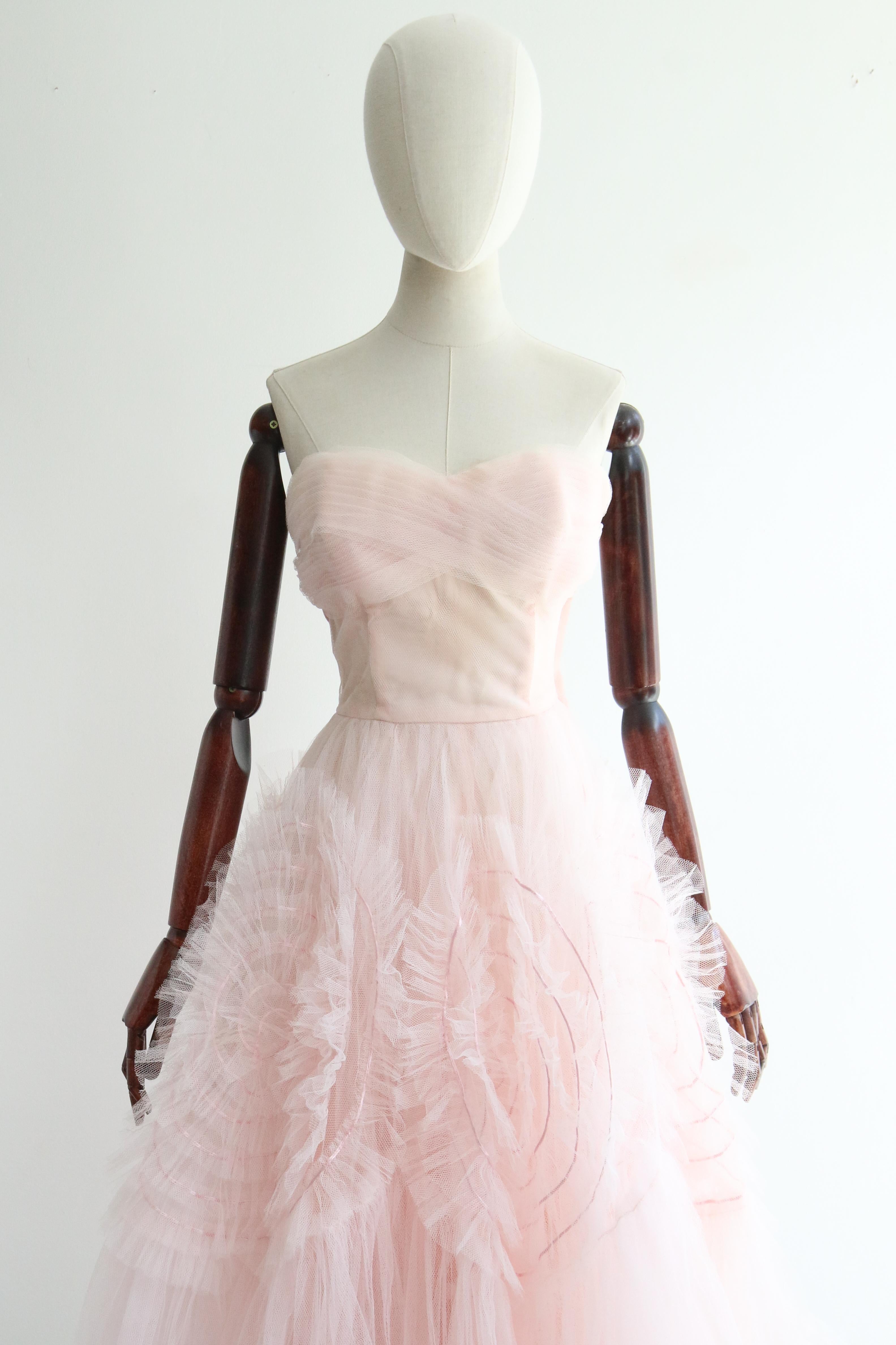 Dieses kultige Kleid aus den 1950er Jahren aus rosa Tüll mit zarten, kreisrunden Satindetails ist genau das Richtige für einen besonderen Anlass. 

Der trägerlose Schnitt des Kleides hat einen herzförmigen Ausschnitt, der von einer Bordüre aus