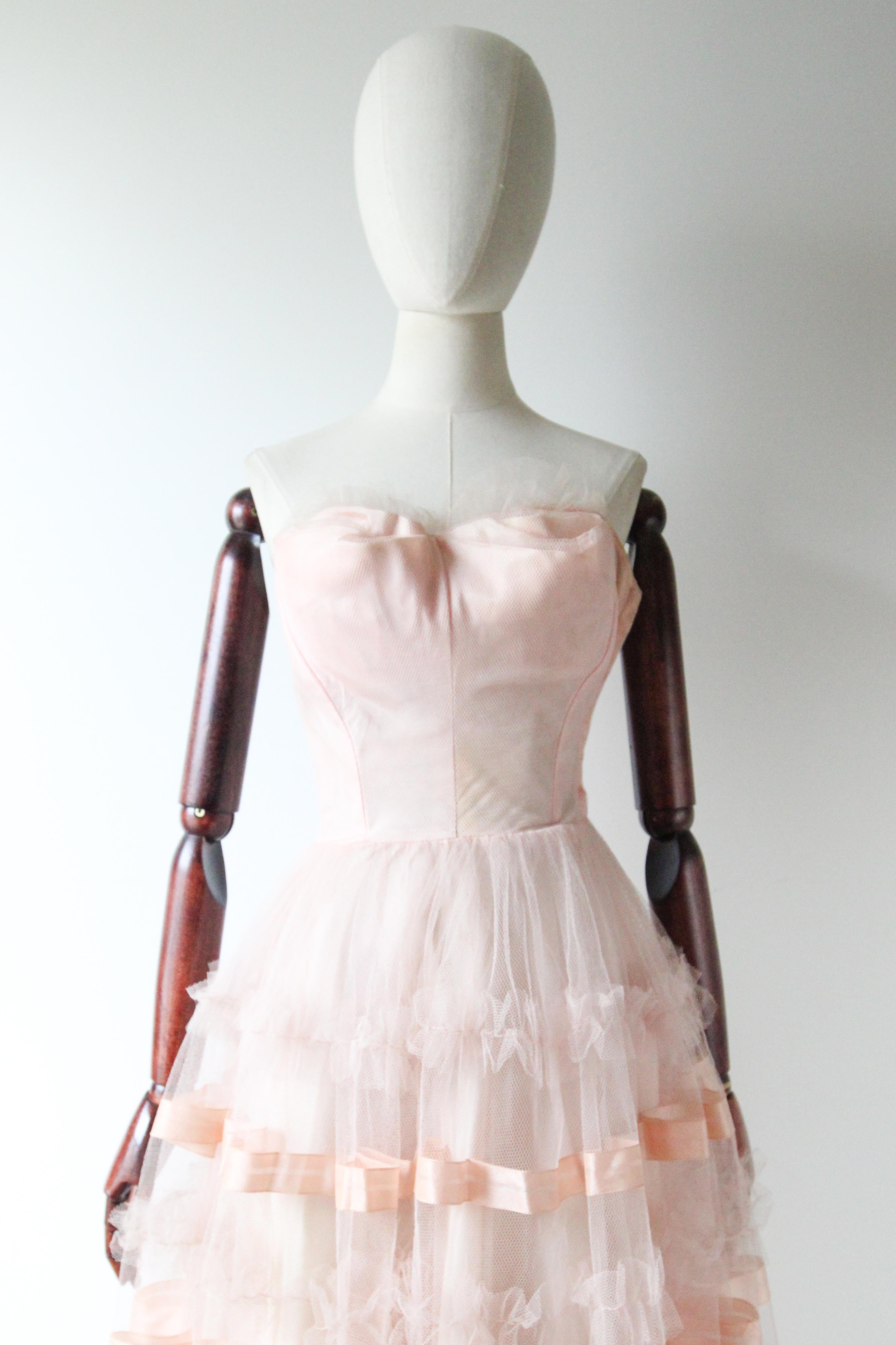 This timeless and iconic 1950's dress, in a ballerina pink layered tulle, with delicate sewn ribbon accents, is the perfect piece for any special occasion.

The strapless neckline of the dress, features a sweetheart décolletage, which is accented by