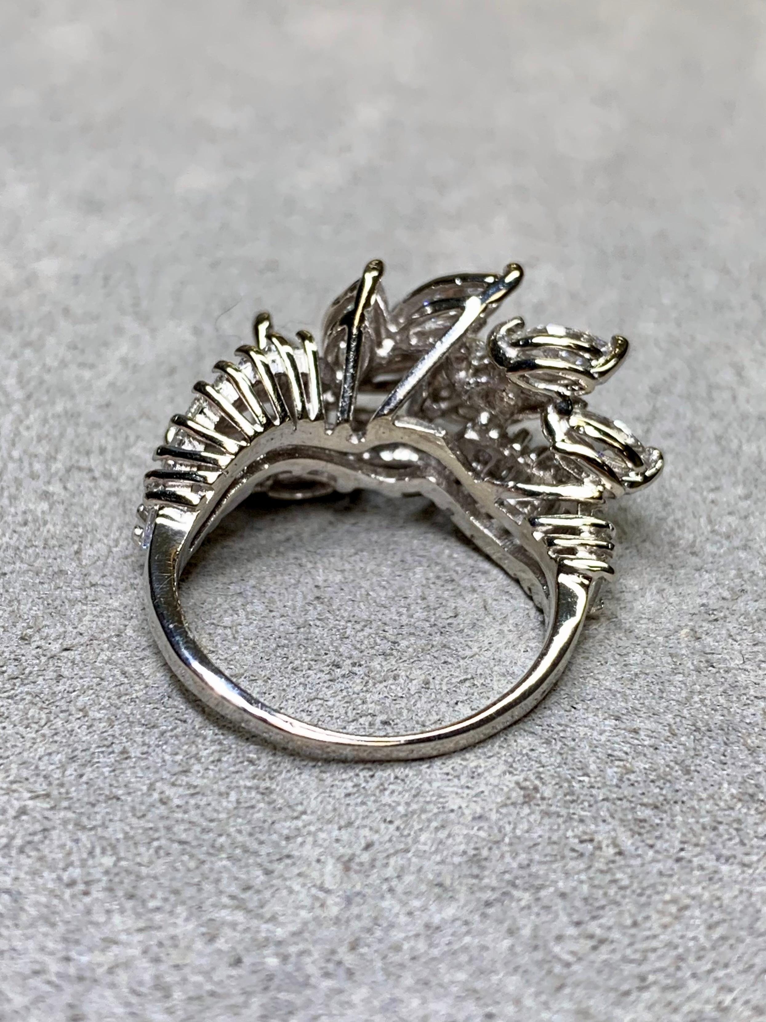 Cette élégante bague de cocktail des années 1950 illustre le glamour du design du milieu du siècle. Réalisée en platine par des experts, cette bague présente un large éventail de diamants de taille marquise et baguette, sertis pour créer un motif