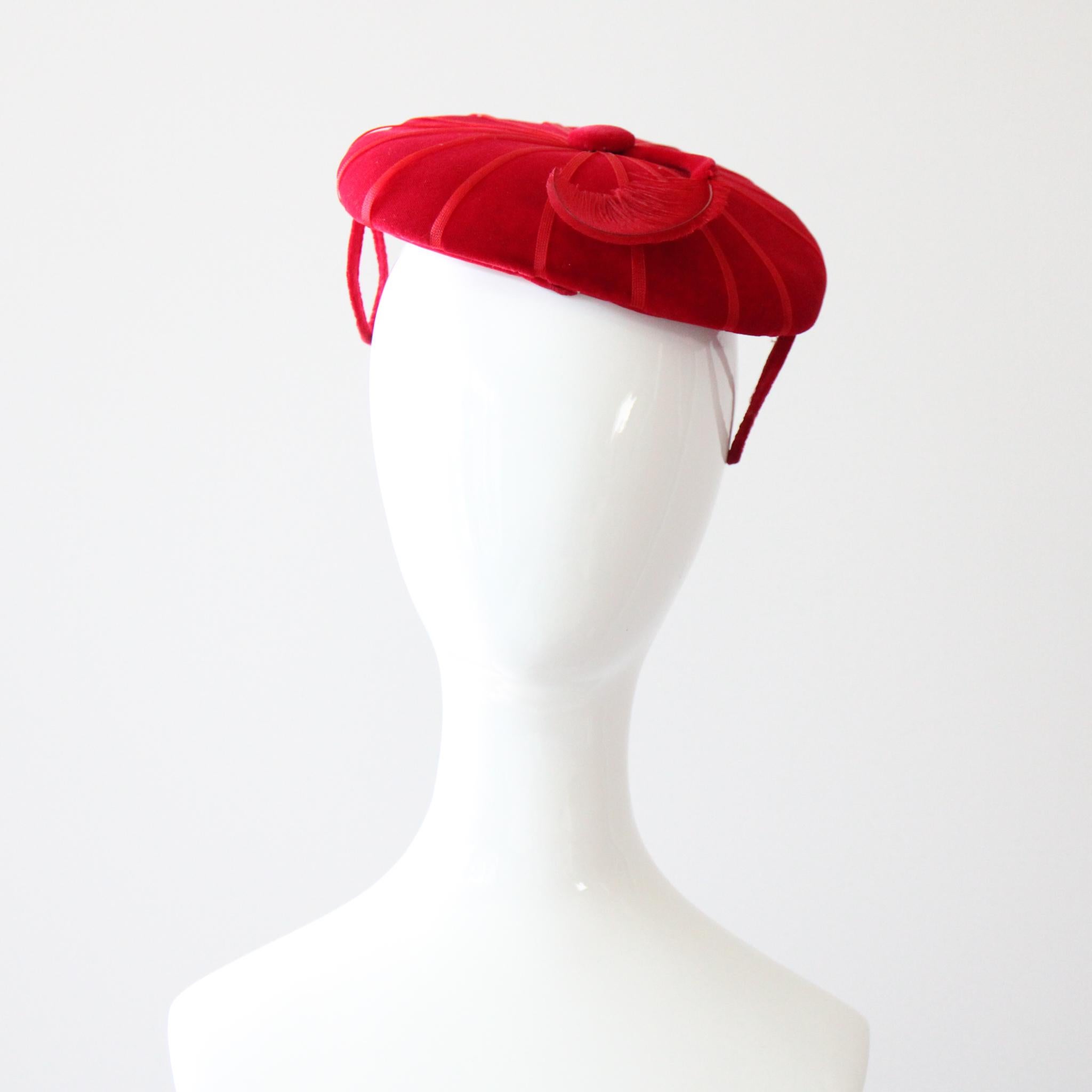 Questo incantevole cappello da percher degli anni '50, realizzato in velluto rosso rubino, impreziosito da un nastro di organza rosso e rifinito con una piuma rossa arricciata, è il pezzo perfetto per completare il tuo abbigliamento. La forma