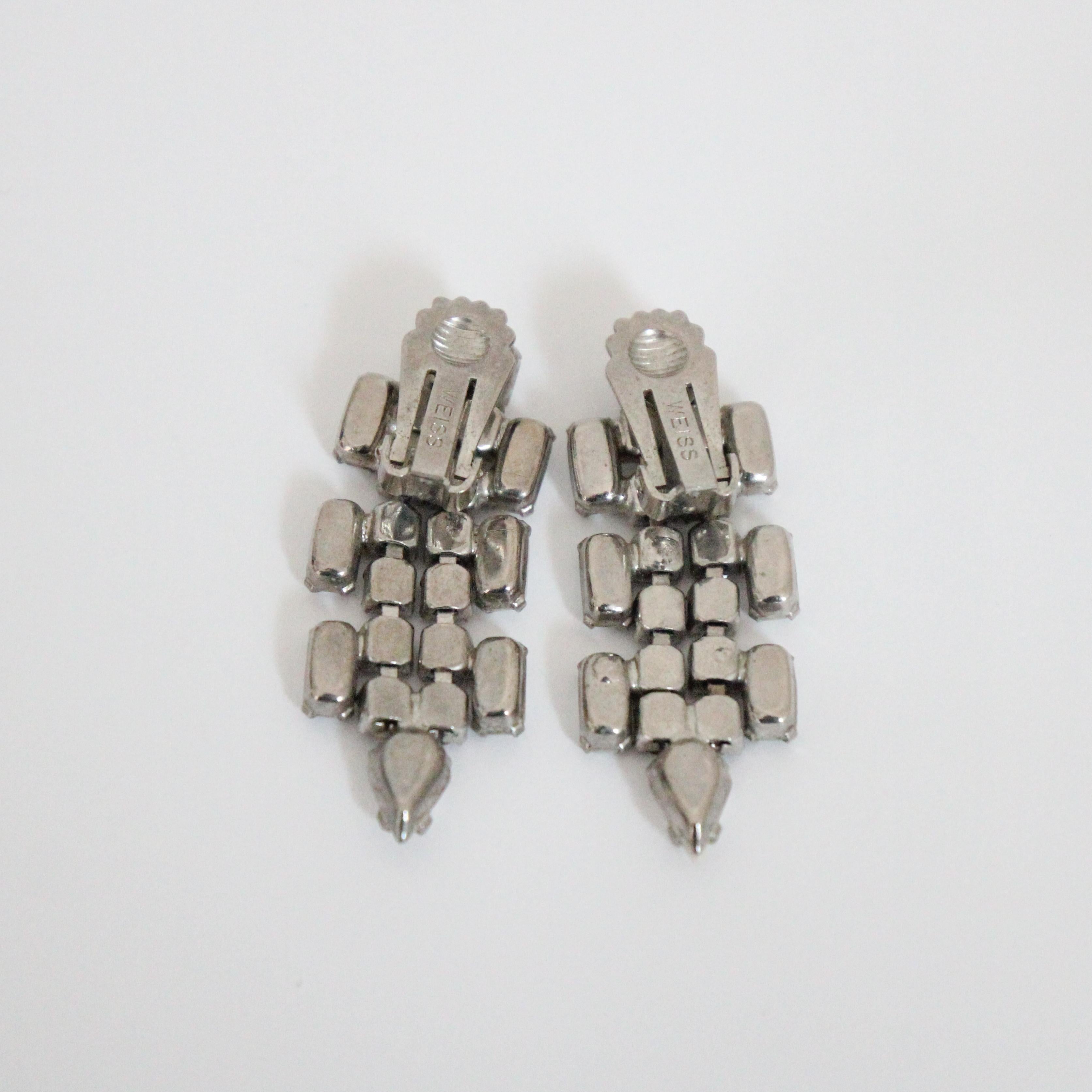 This breathtaking pair of 1950's clip on earrings, on silver toned metal bases, made up of baguette cut and teardrop cut claw set milk glass stones, surrounding silver claw set rhinestones, in a chandelier design, are the perfect touch of sparkle to