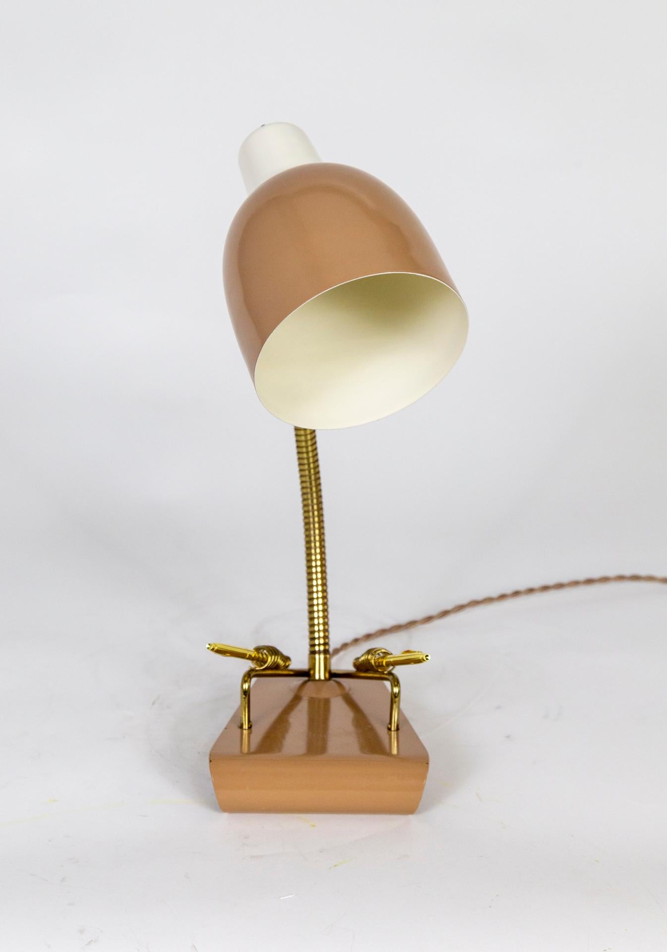 A Mid-Century Modern desk lamp with an angled, curled-under base that has two coiled, brass pen holders; echoing the brass, adjustable, hose neck. The base and shade are lacquered in a rich, latte or mushroom tone, with white accent. Push switch;