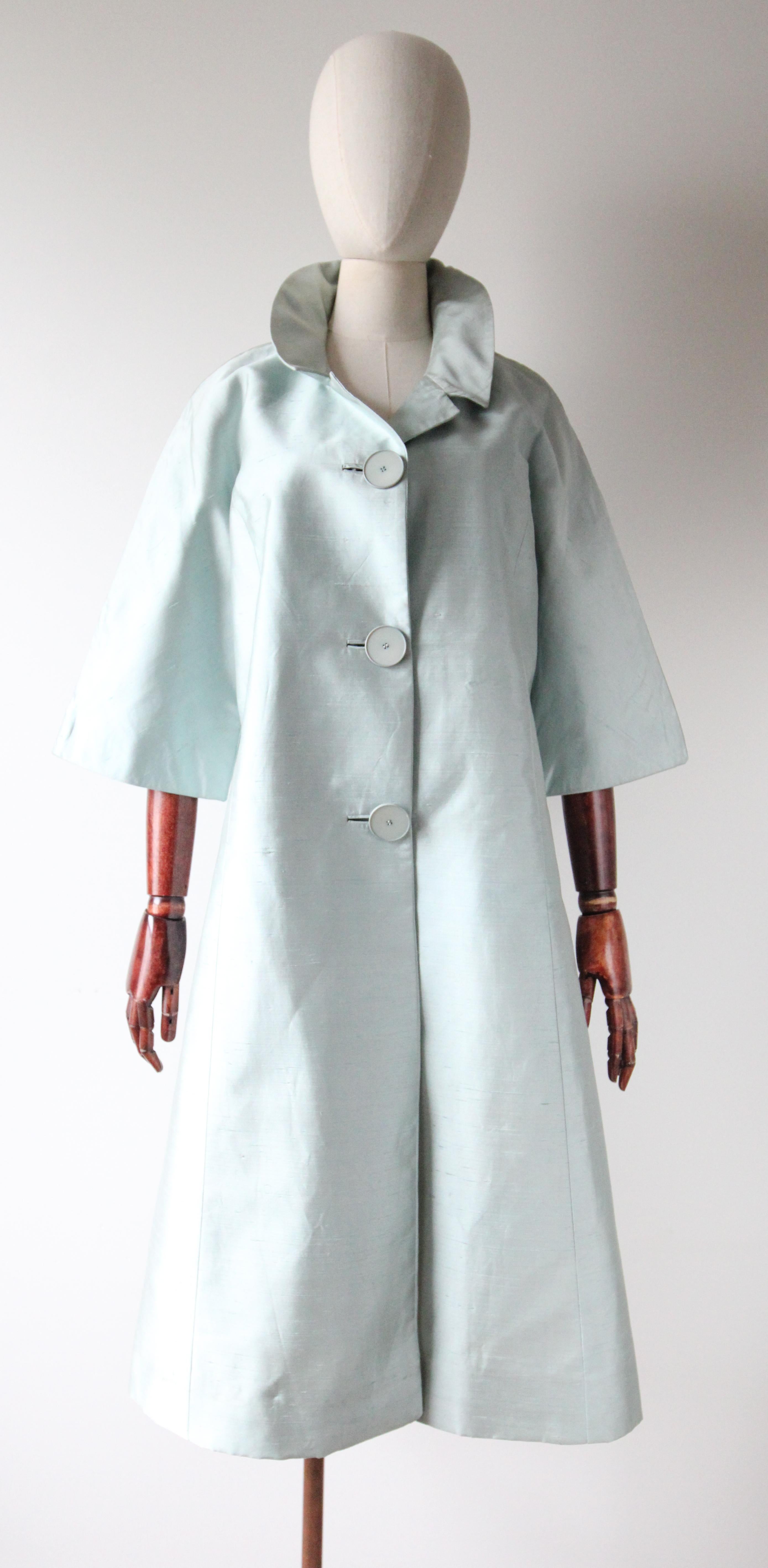 Dieser originale Shantung-Seidenmantel aus den 1950er Jahren in einem zarten Eisblauton ist die perfekte Ergänzung für Ihre Vintage-Sammlung. 

Der V-förmige Ausschnitt wird von einem abgerundeten und gekerbten Kragen umrahmt, der sich mit einem