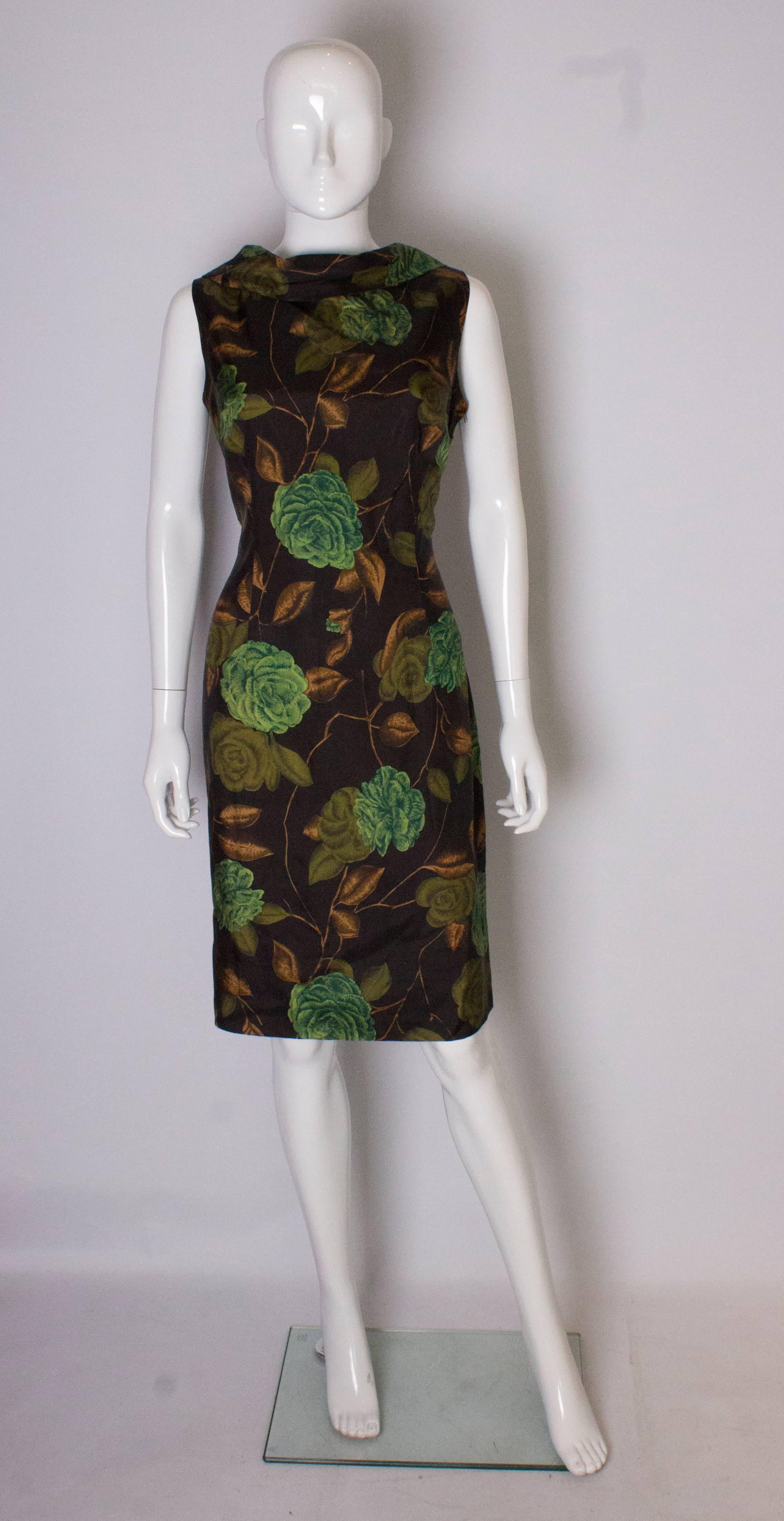 A vintage Marldena, 1950s wiggle shift dress. The dress has  a cowl neck at the front and v neck at the back. It is  in a brown fabric, with  a green and brown flower print, and has a side zip opening.