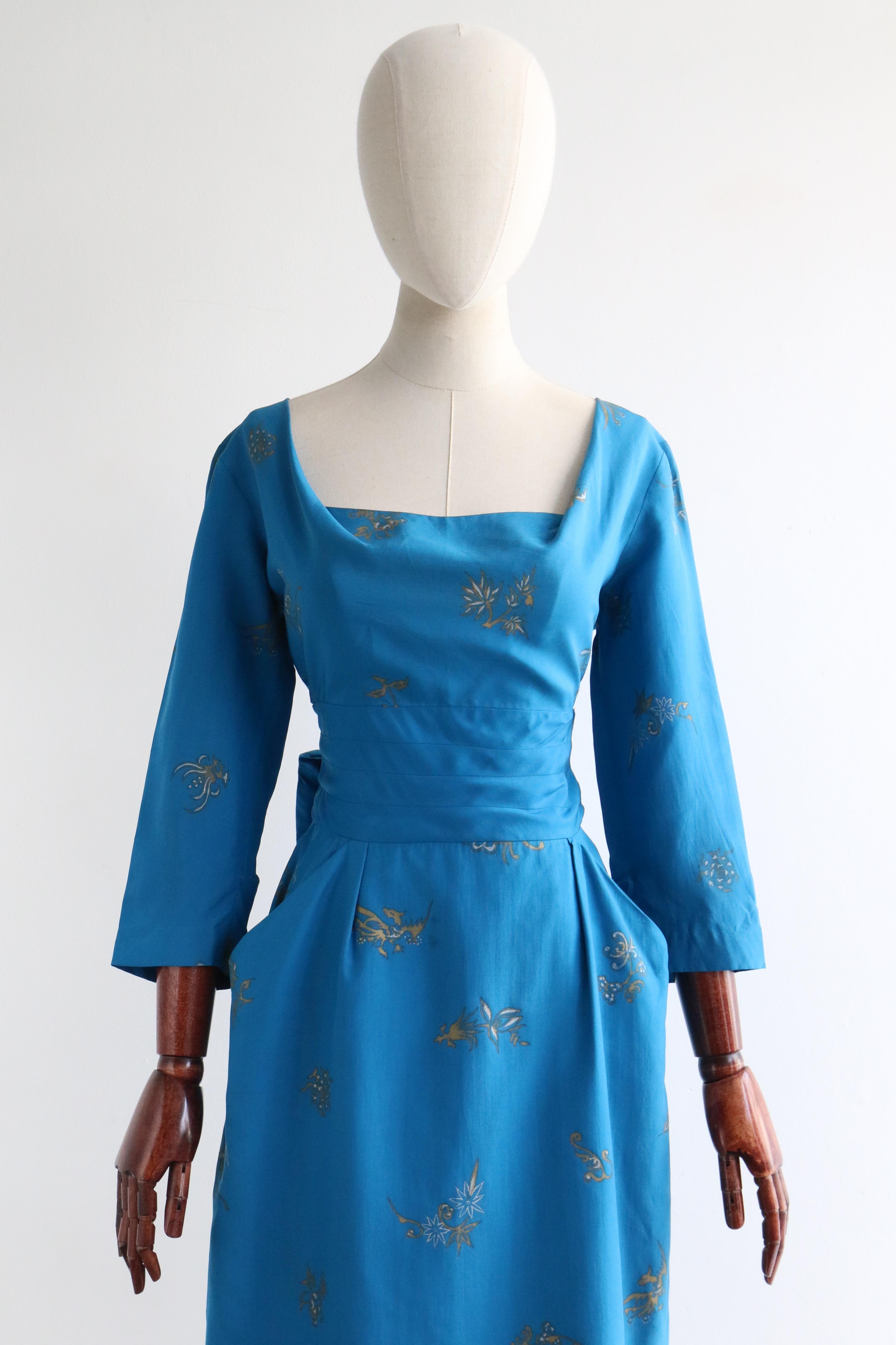 This collectible and truly magnificent 1950's dress by Alfred Shaheen, rendered in the most vibrant shade of aqua blue silk, with a gold and white toned floral and bird print, is just the piece to welcome the new season with.

 The rounded neckline