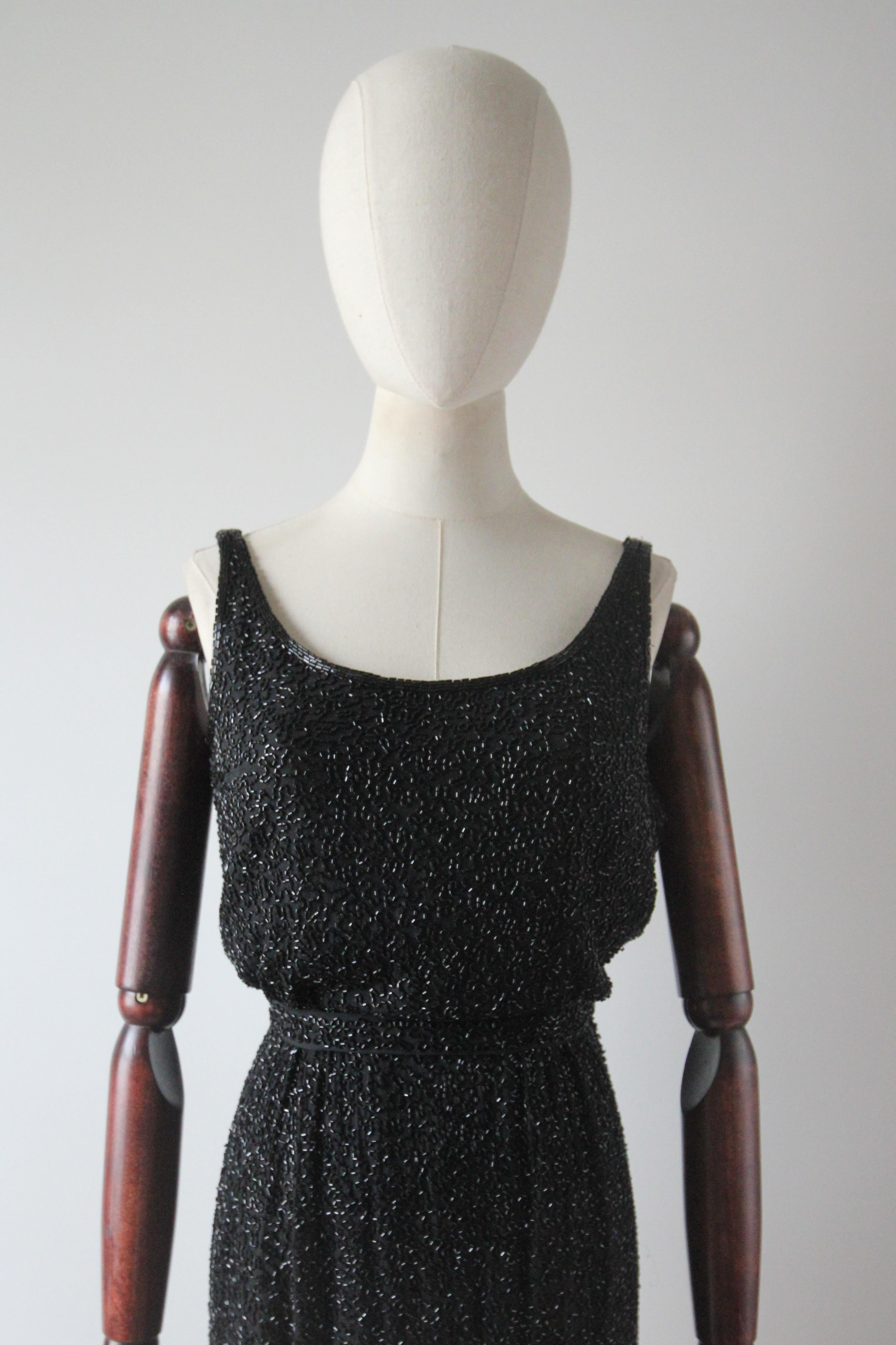 Rendered in an iconic and breathtaking silhouette, this original 1950's cocktail dress rendered in a black silk and embellished with trailing black glass beadwork, is the perfect piece to dazzle with.
 
The elegant rounded neckline, is framed by a