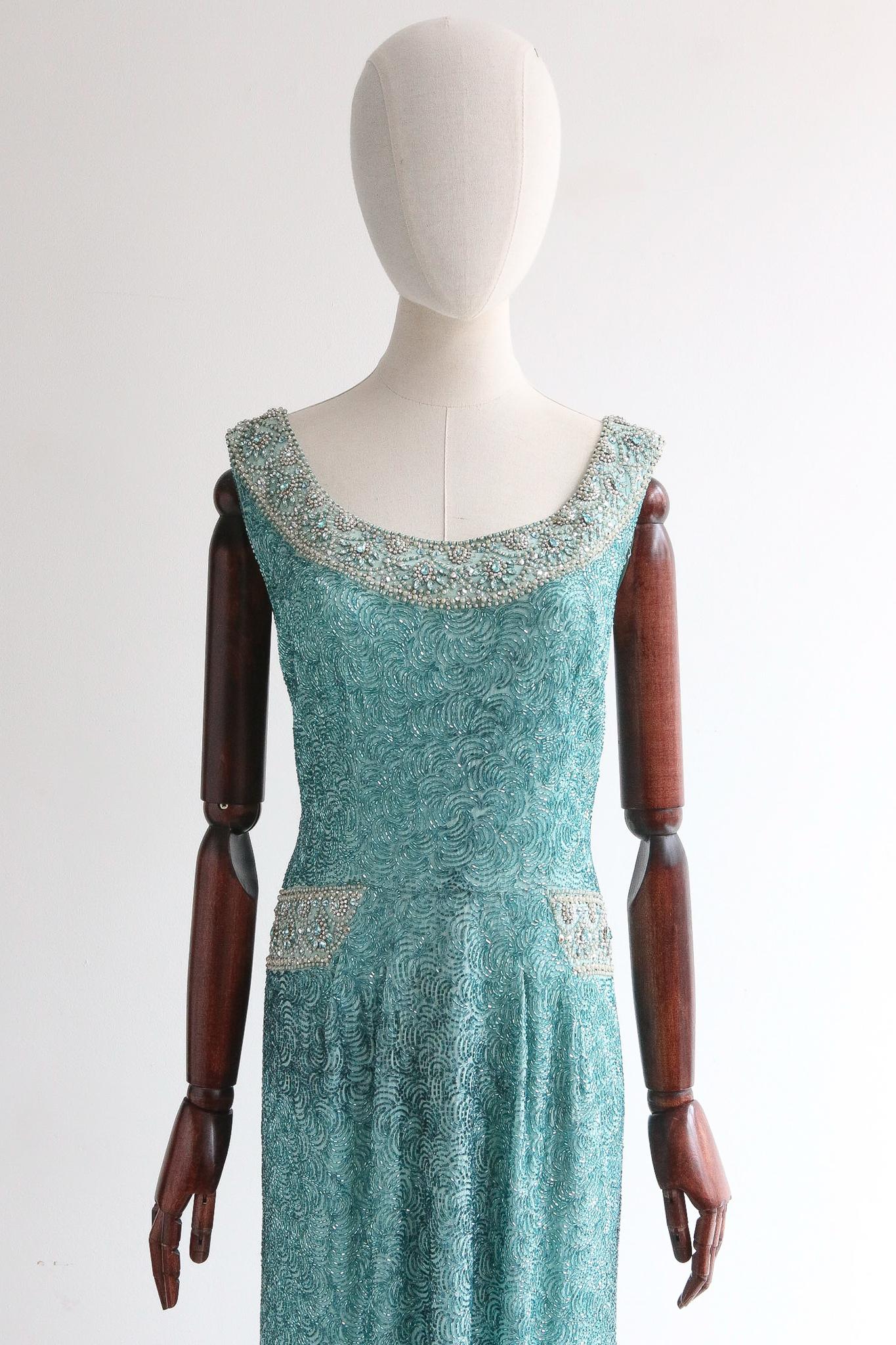 This breathtaking late 1950's Norman Hartnell cocktail dress, on a silk base and fully embellished with trailing glass beadwork, glass rhinestones and pearlised bead accents is a rare piece of history to behold. 

The rounded neckline is framed by a