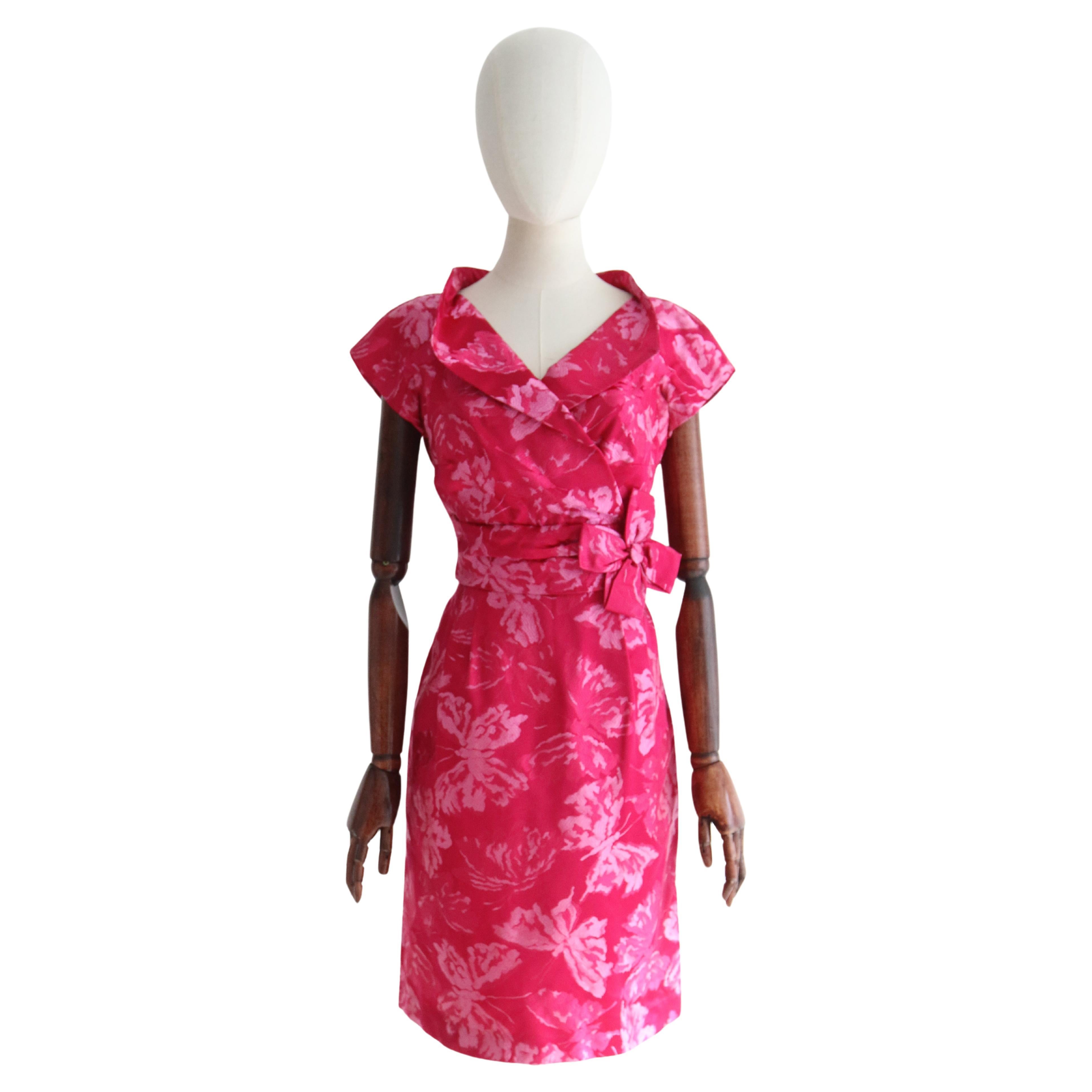 Una maravilla para la vista, este original vestido de brocado de seda de los años 50 en un vibrante tono rosa fucsia con toques rosa, en un maravilloso e intrincado estampado de mariposas, es justo la pieza que debes añadir a tu colección vintage.  