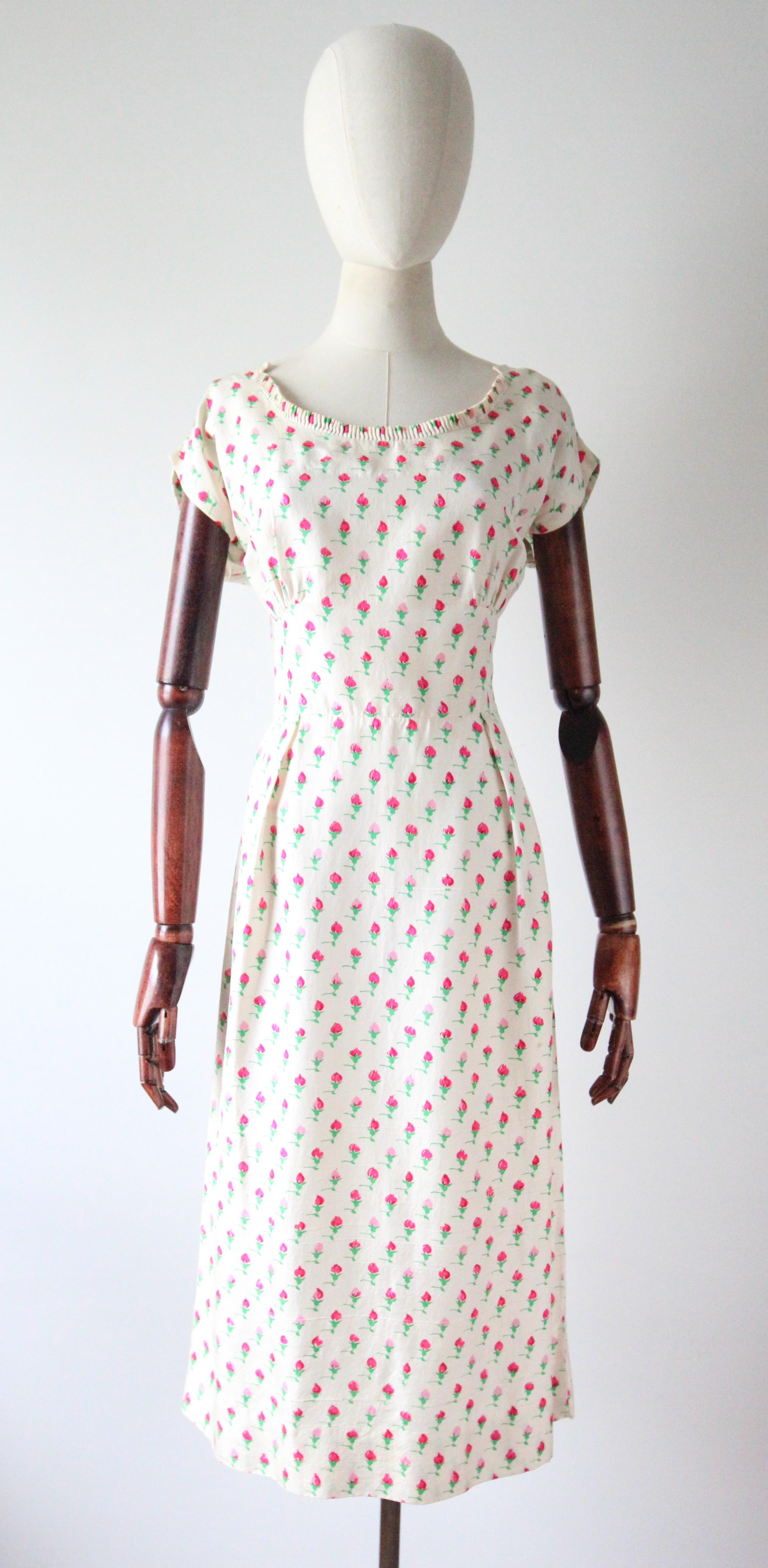 Rendered in the most sumptuous raw silk with a pattern of rose buds in shades of pink with bold green stems, accented by delicate pleated details and velvet finishings, this original 1950's dress and jacket set is just the piece to add to your