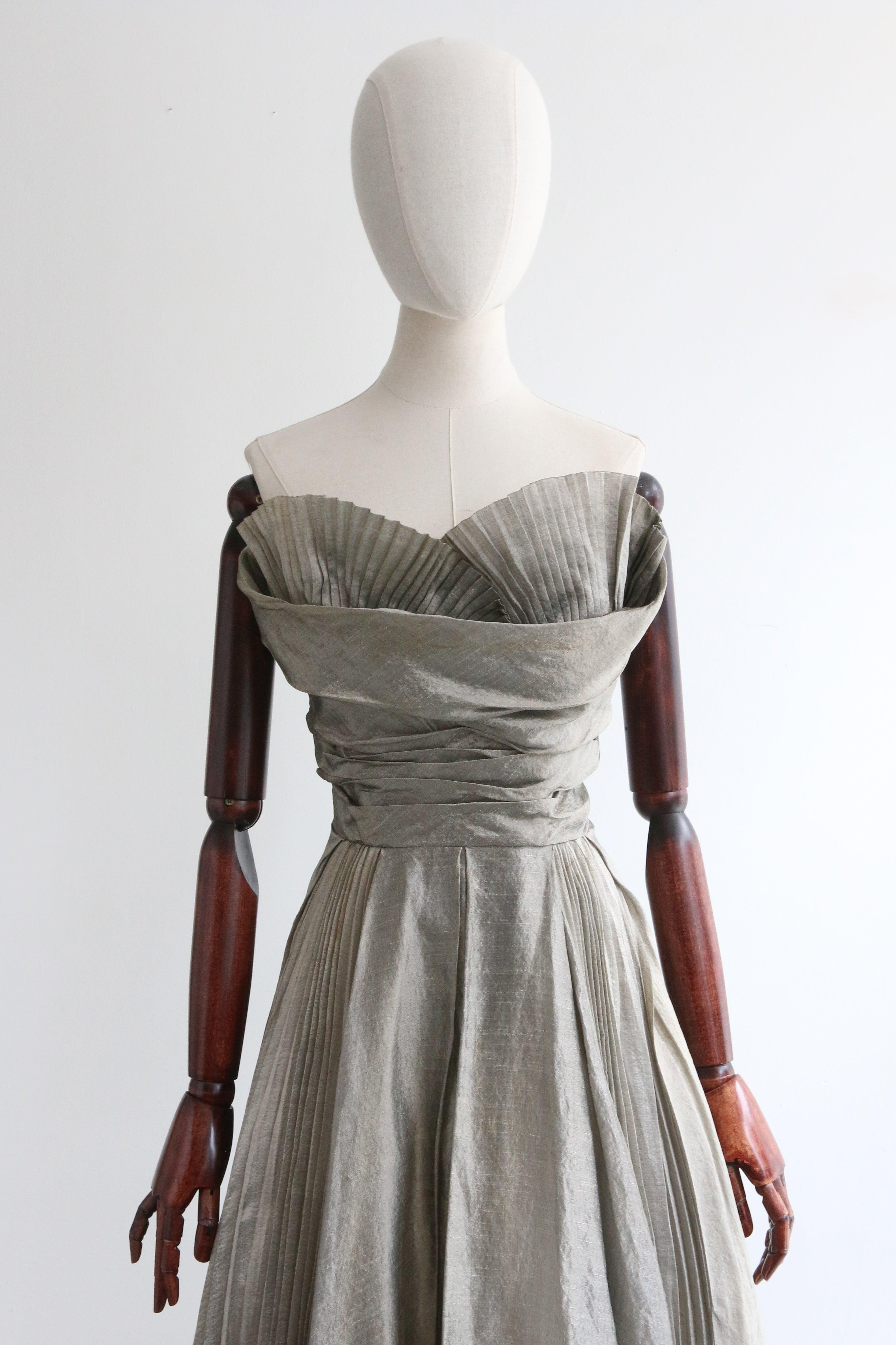 Dieses spektakuläre Kleid aus silberfarbenem Seidenorganza aus den 1950er Jahren ist das perfekte Stück für Ihre Cocktailgarderobe. 
Der trägerlose Schnitt des Kleides wird durch einen herzförmigen Ausschnitt akzentuiert, der durch strahlende,